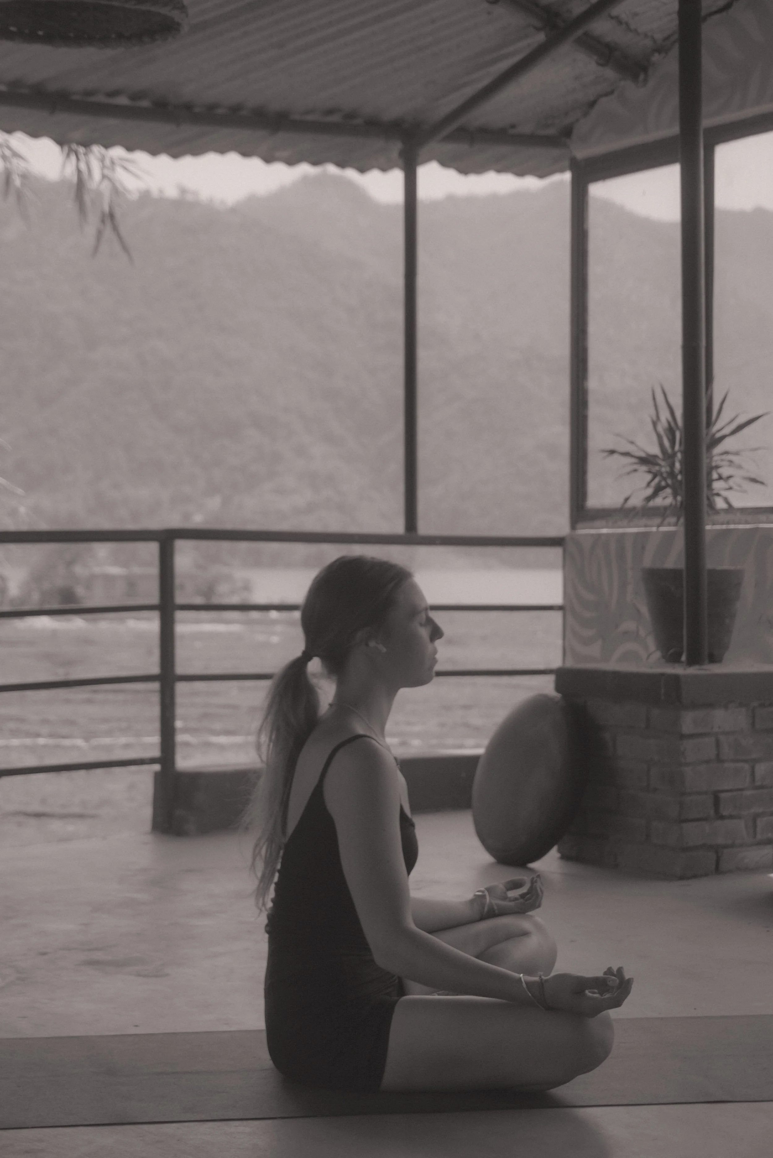 A woman practicing yoga in a seated meditation pose on a mat, outdoors with a mountain view in the background.