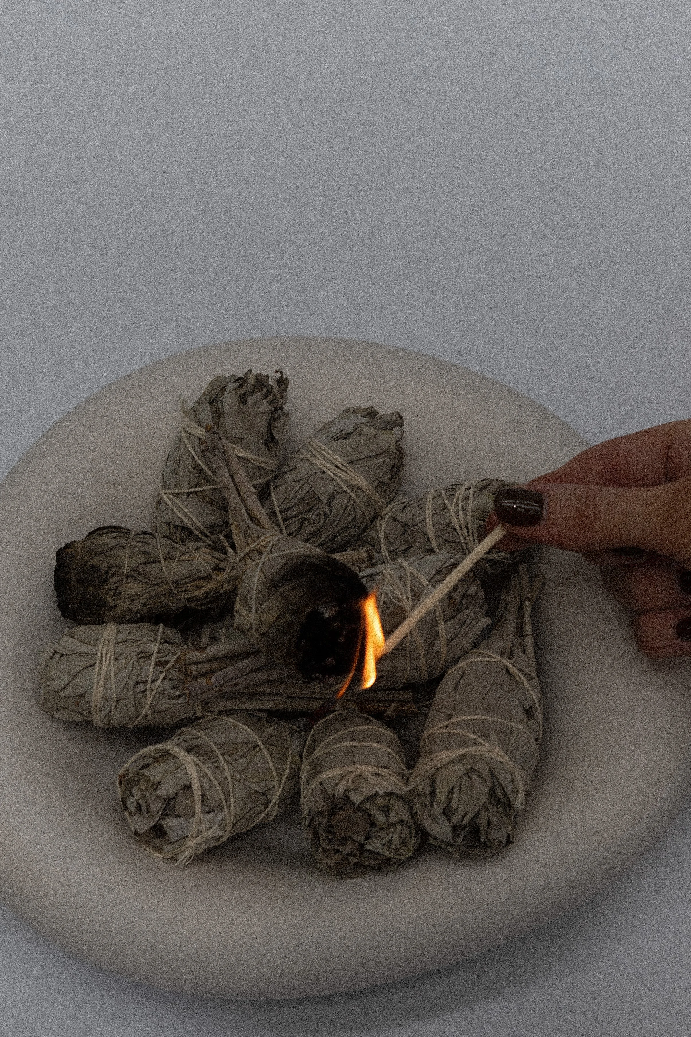 Person lighting a bundle of sage with a match where the sage is on a white dish.