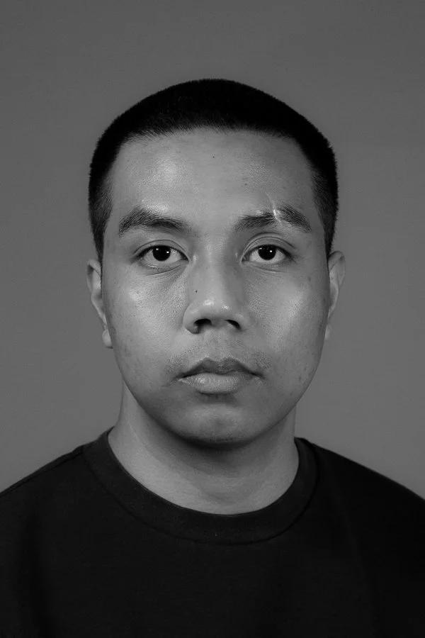 Black and white portrait of a man with short hair wearing a dark shirt, looking directly at the camera with a neutral expression.