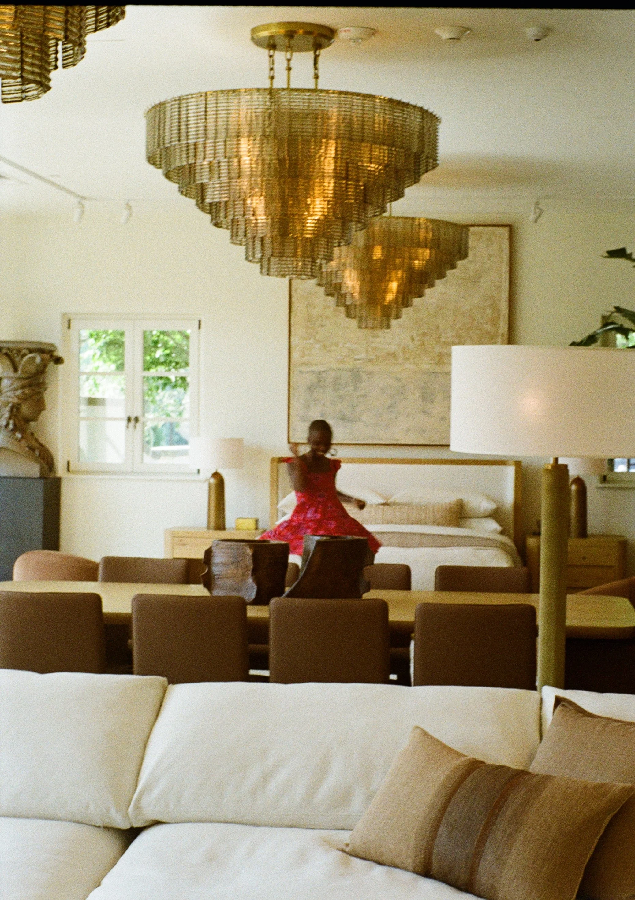 A woman in a red dress sitting on a bed in a bedroom with modern lighting and decor.