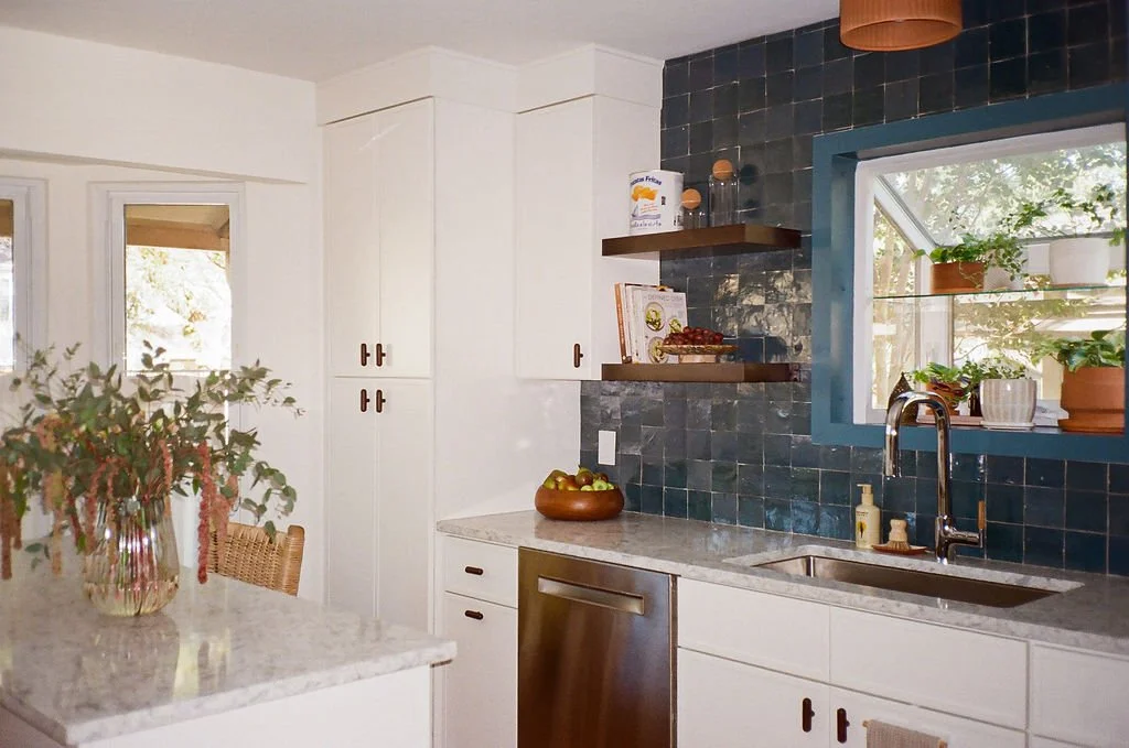 The Modern Mediterranean kitchen in Austin, Texas designed by Jordyn Garcia Studio. It features zellige backsplash tile in Aegean sea tones & terracotta floor. It includes white slim shaker cabinets with walnut hardware, & a custom arched tile niche.