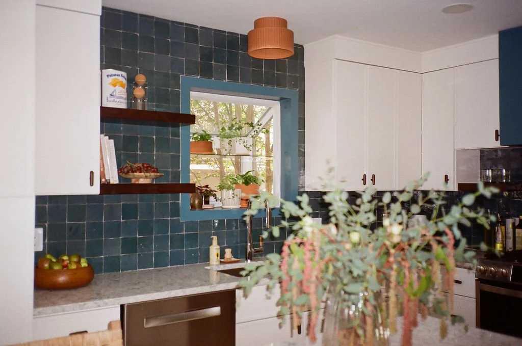 The Modern Mediterranean kitchen in Austin, Texas designed by Jordyn Garcia Studio. It features zellige backsplash tile in Aegean sea tones & terracotta floor. It includes white slim shaker cabinets with walnut hardware, & a custom arched tile niche.