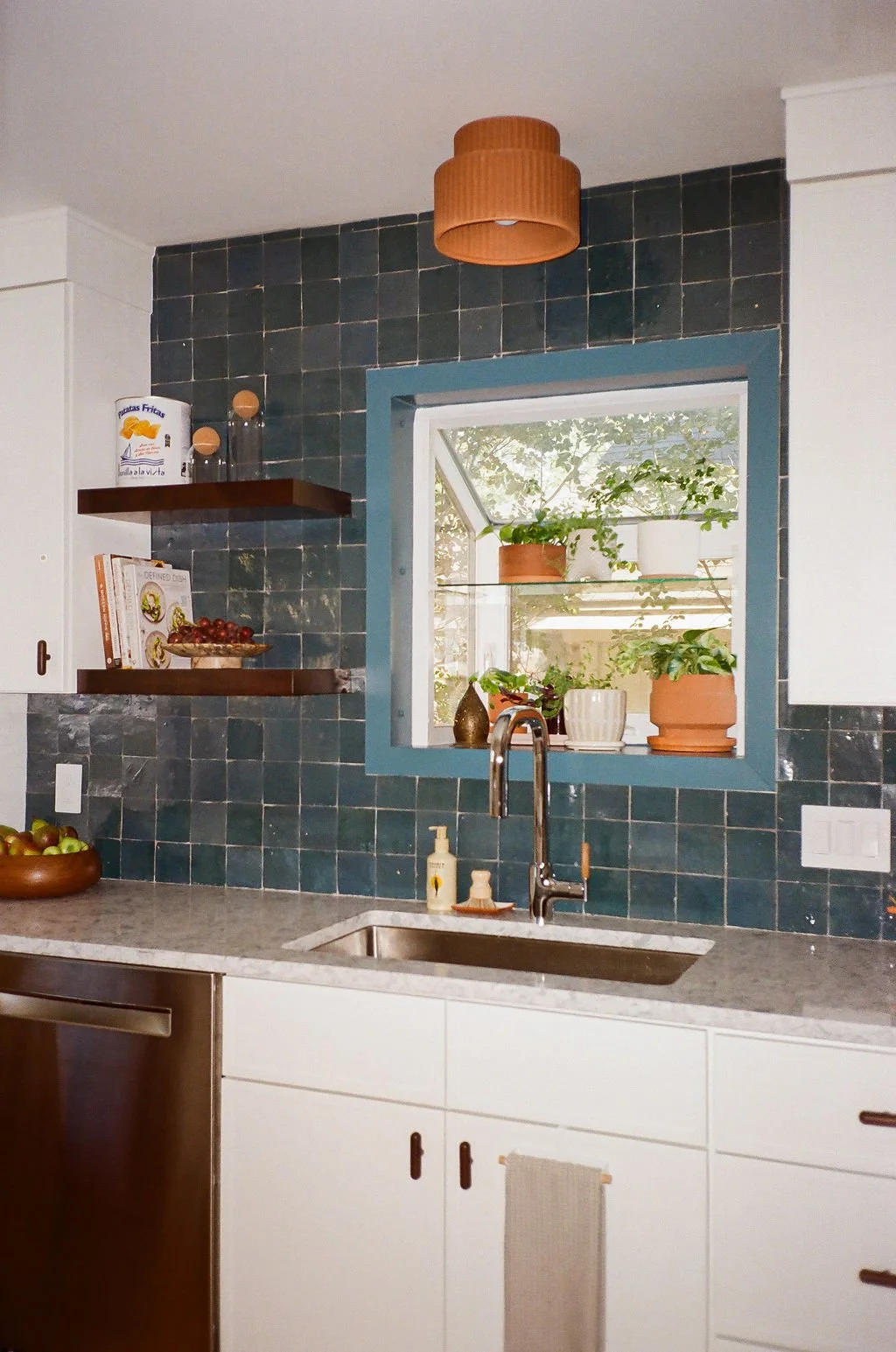 A close-up of the modern chrome faucet with a teak lever, modern quartz countertops, and a garden window above the kitchen sink in Jordyn Garci Studio's Modern Mediterranean Kitchen remodel in Austin, Texas.