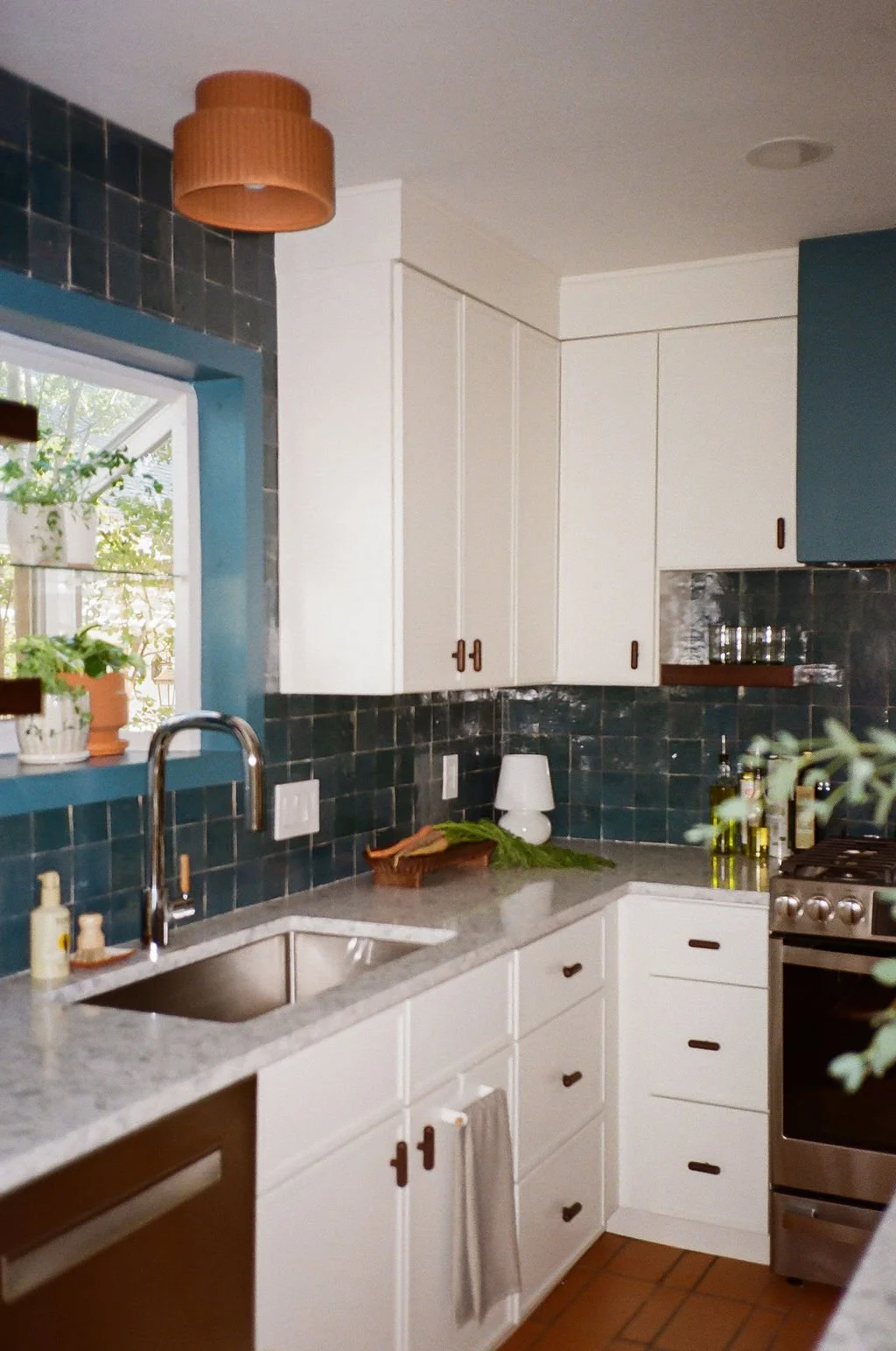 The Modern Mediterranean kitchen in Austin, Texas designed by Jordyn Garcia Studio. It features zellige backsplash tile in Aegean sea tones & terracotta floor. It includes white slim shaker cabinets with walnut hardware, & a custom arched tile niche.