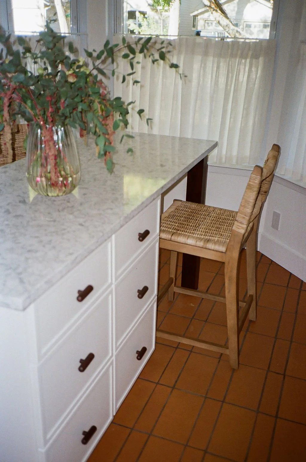 A close up of the terracotta floor tiles in Jordyn Garcia Studio's Modern Mediterranean kitchen. The floor tile pattern includes mixing two different tile sizes to create a modern grid pattern. The custom island includes walnut square legs.