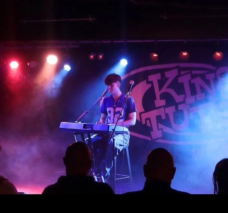 A cartoon donut character wearing high-heeled shoes, sunglasses, and a graduation cap, holding a microphone, with a skull and musical notes above it, and the letters 'GMS' below.