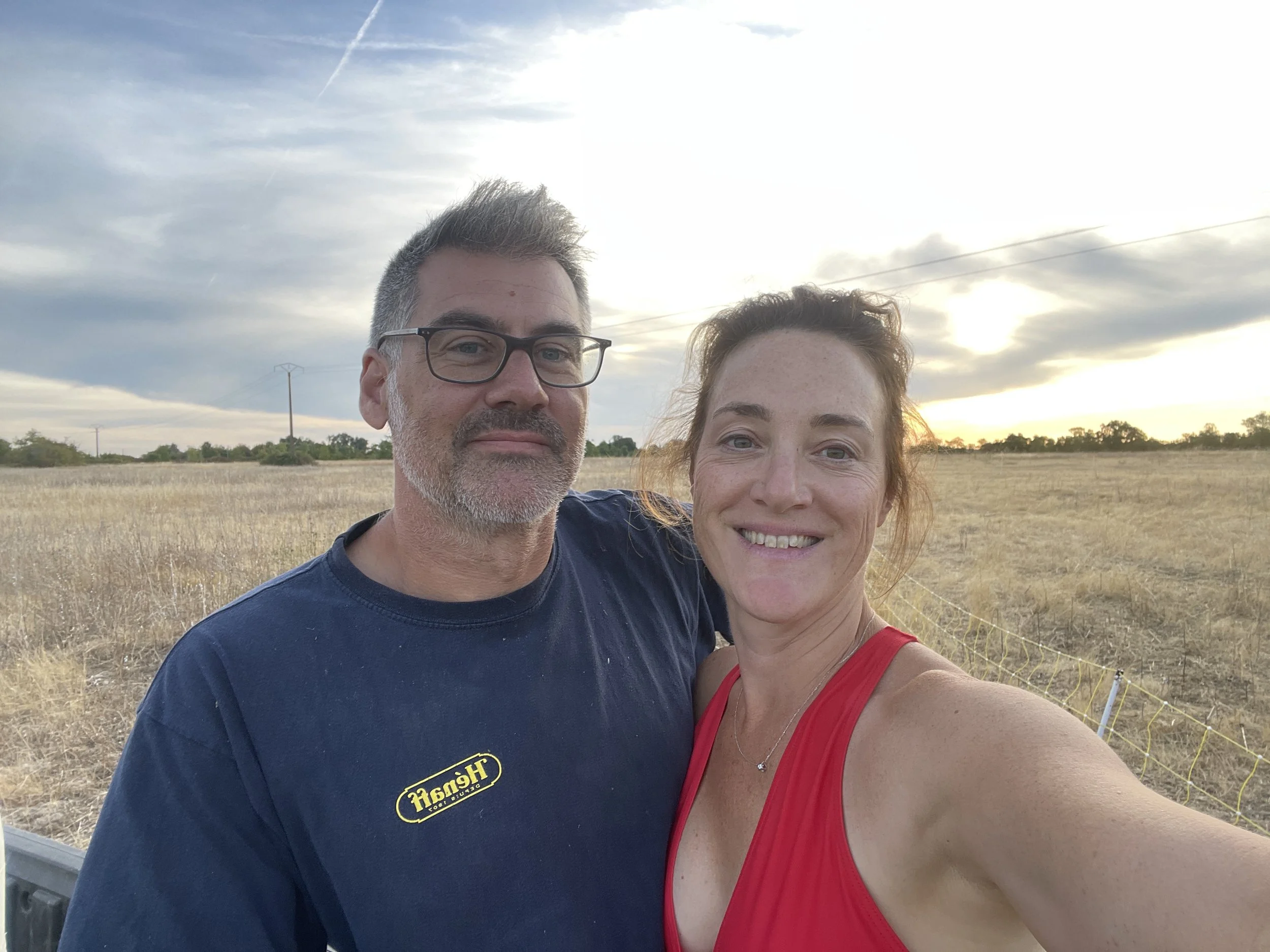 Portrait de Pauline et Lionel, les vignerons du Domaine des Grouas dans un champ, avec un coucher de soleil en arrière-plan.