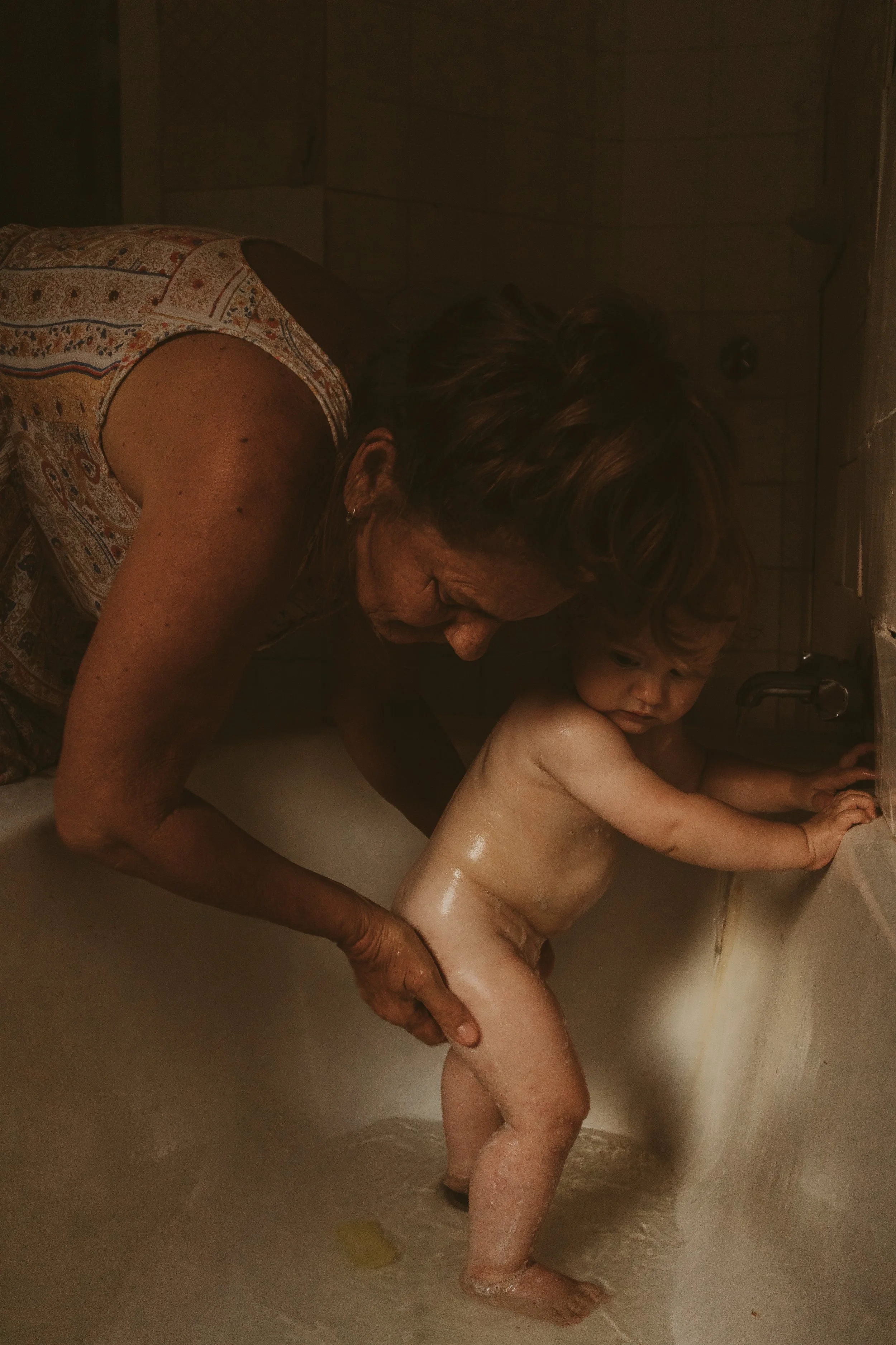 Motherhood photography. Family photography. Baby getting washed by grandma in rustic bath.