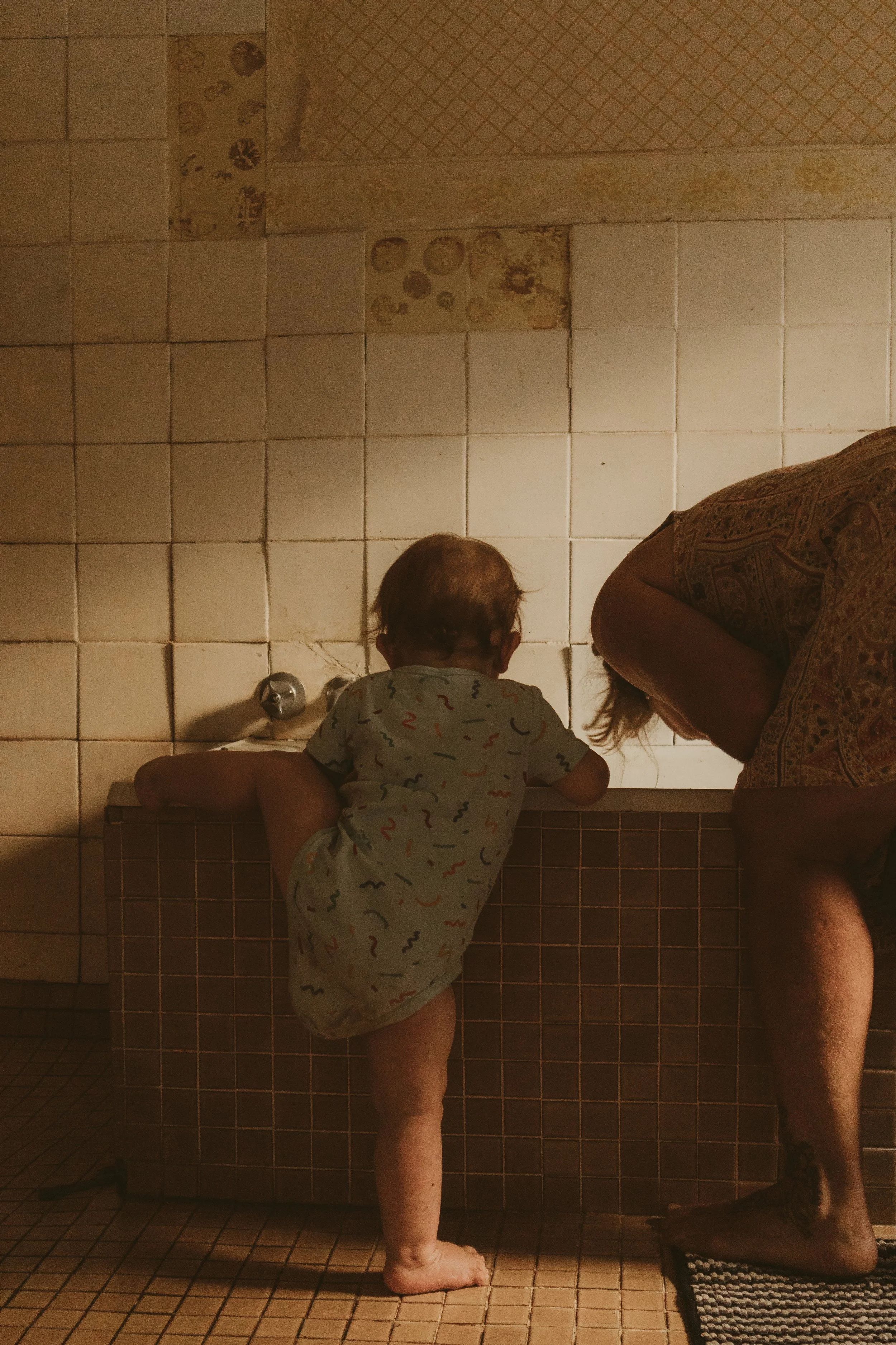 Motherhood photography. Baby climbing into bath in rustic bathroom. Family photograpy. In-home photography.