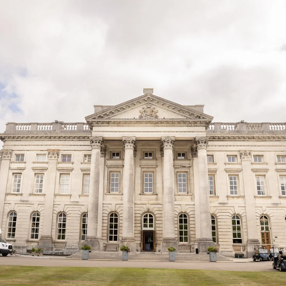 A neoclassical grand government or institutional building with tall columns and a triangular pediment, cloudy sky in the background.