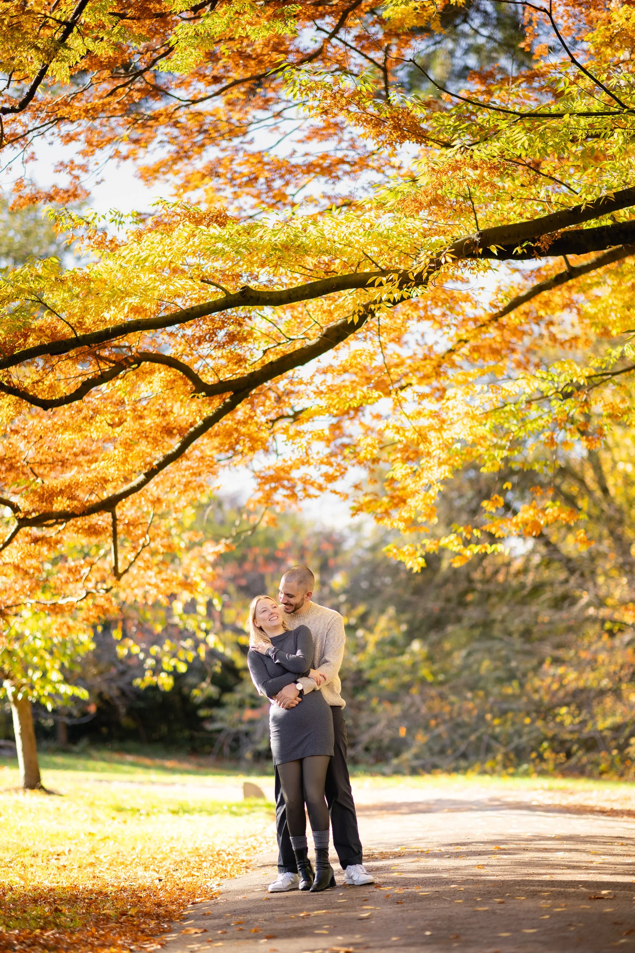 A couple enjoying the fall season under colorful autumn leaves in a park.