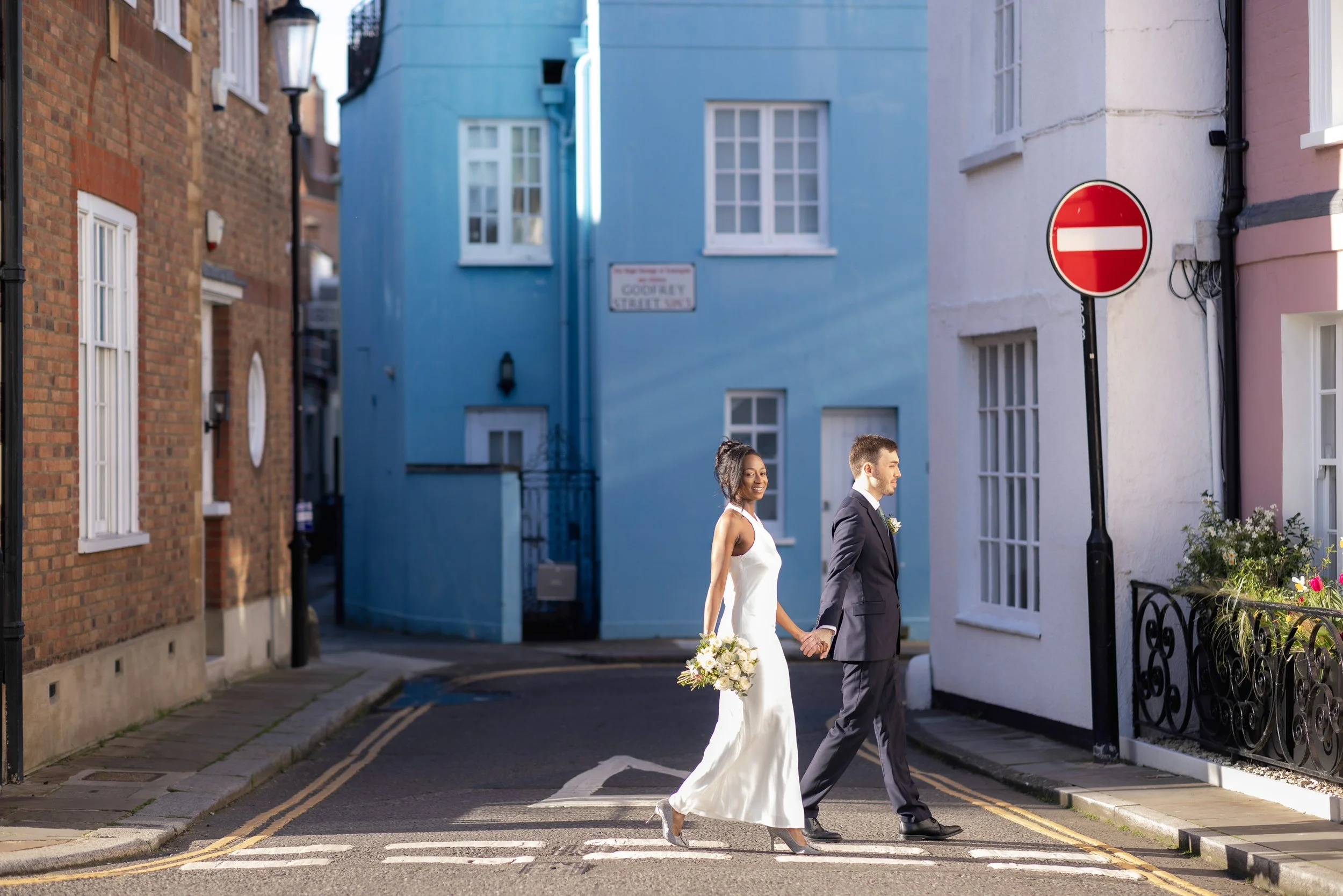 A bride and groom walking hand in hand across a crosswalk in a colorful city street.