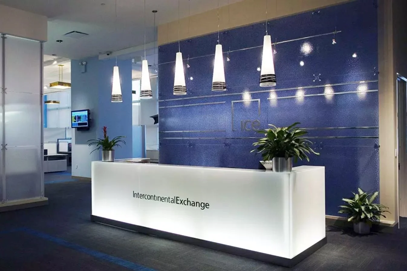 Intercontinental Exchange - ICE's modern lobby designed by BGA  features an illuminated front desk accented with a blue back wall and five hanging cylindrical lighting fixtures.