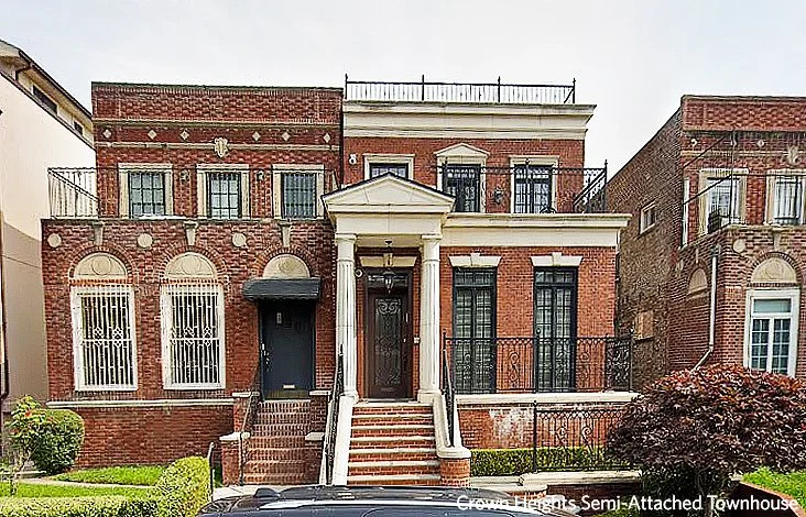 Exterior of a semi-detached Brooklyn townhouse two stories high. Red brick with stairs leading up to the entry mirroring the neighboring house.