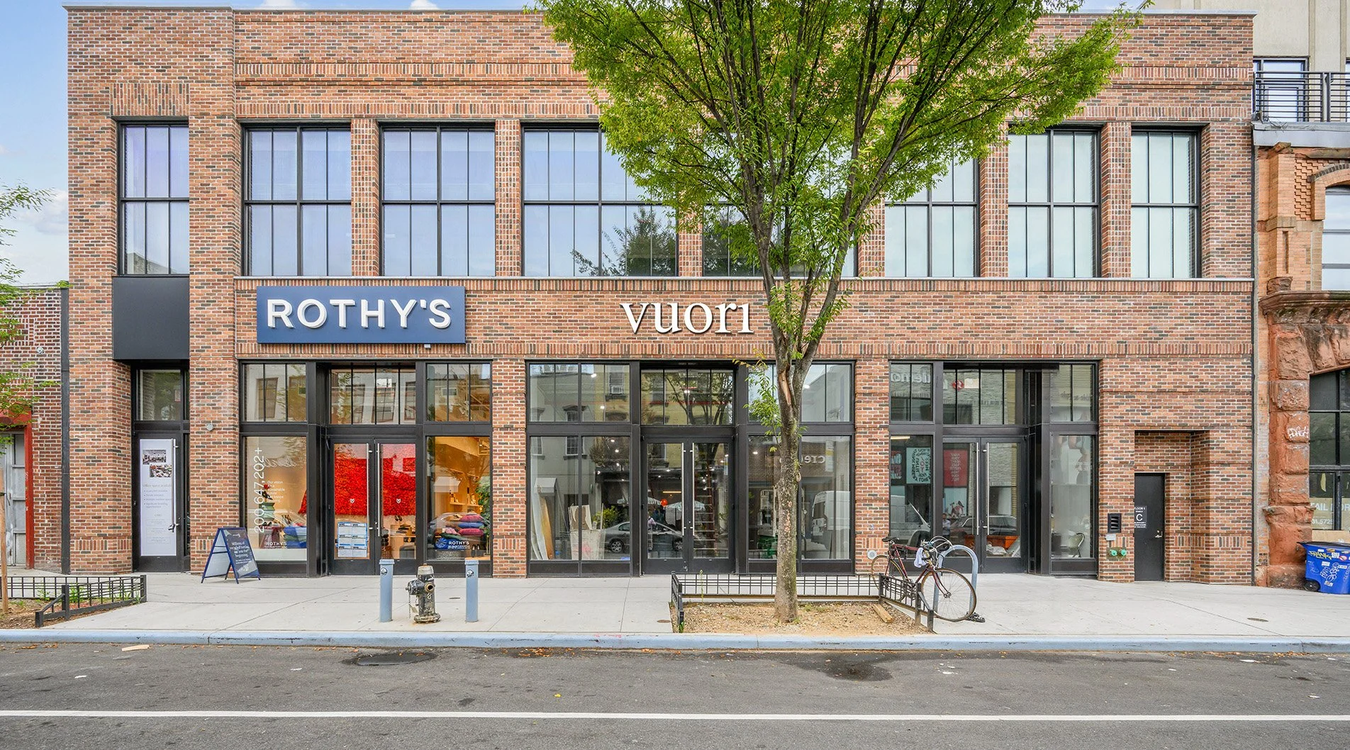 Exterior pale red brick new commercial retail  building with large glass windows for tenants Rothy's and Vuori. Williamsburg, Brooklyn