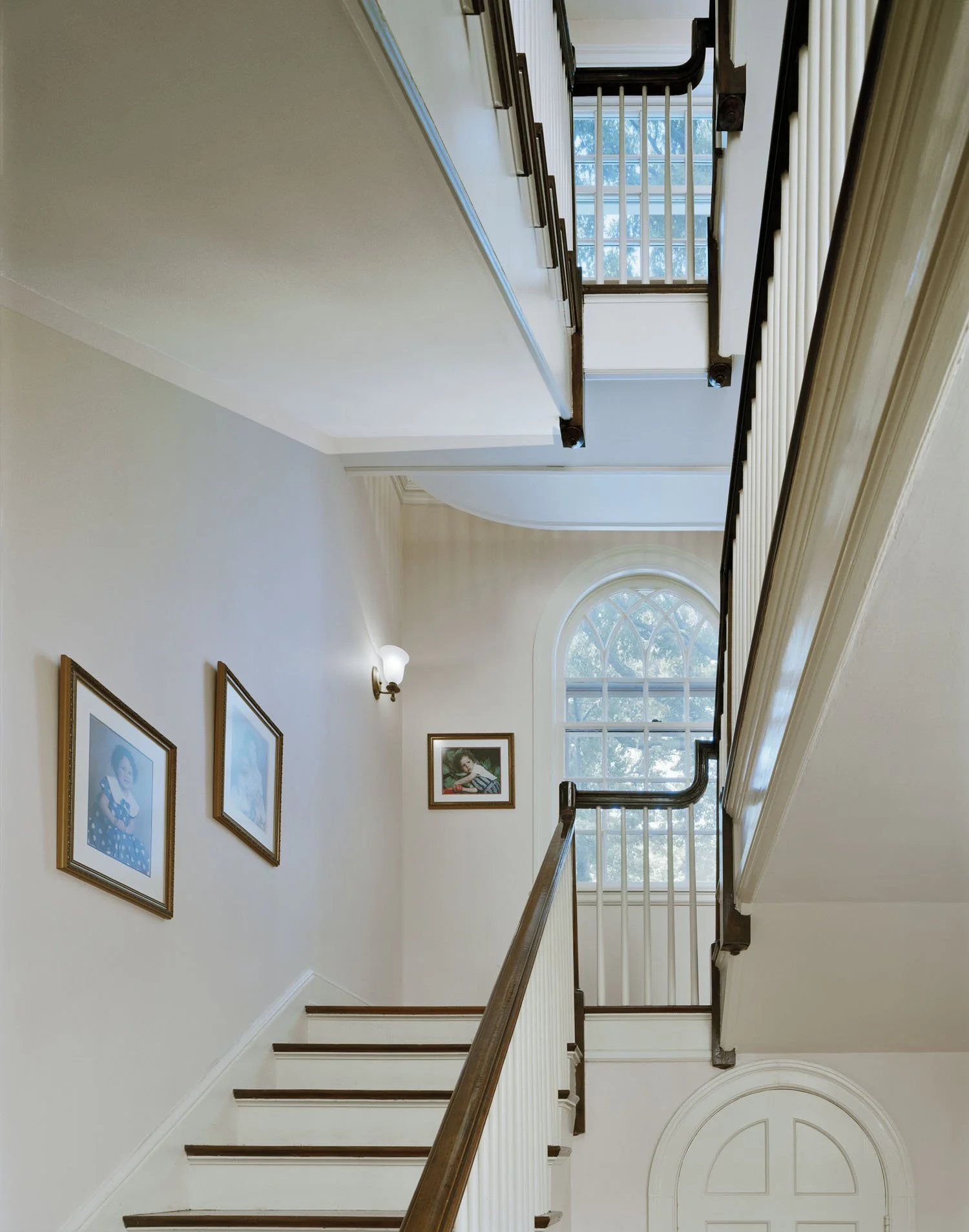 This interior white hallway features two parallel staircases encompassing three entire stories as well as a protruding balcony over the first staircase.
