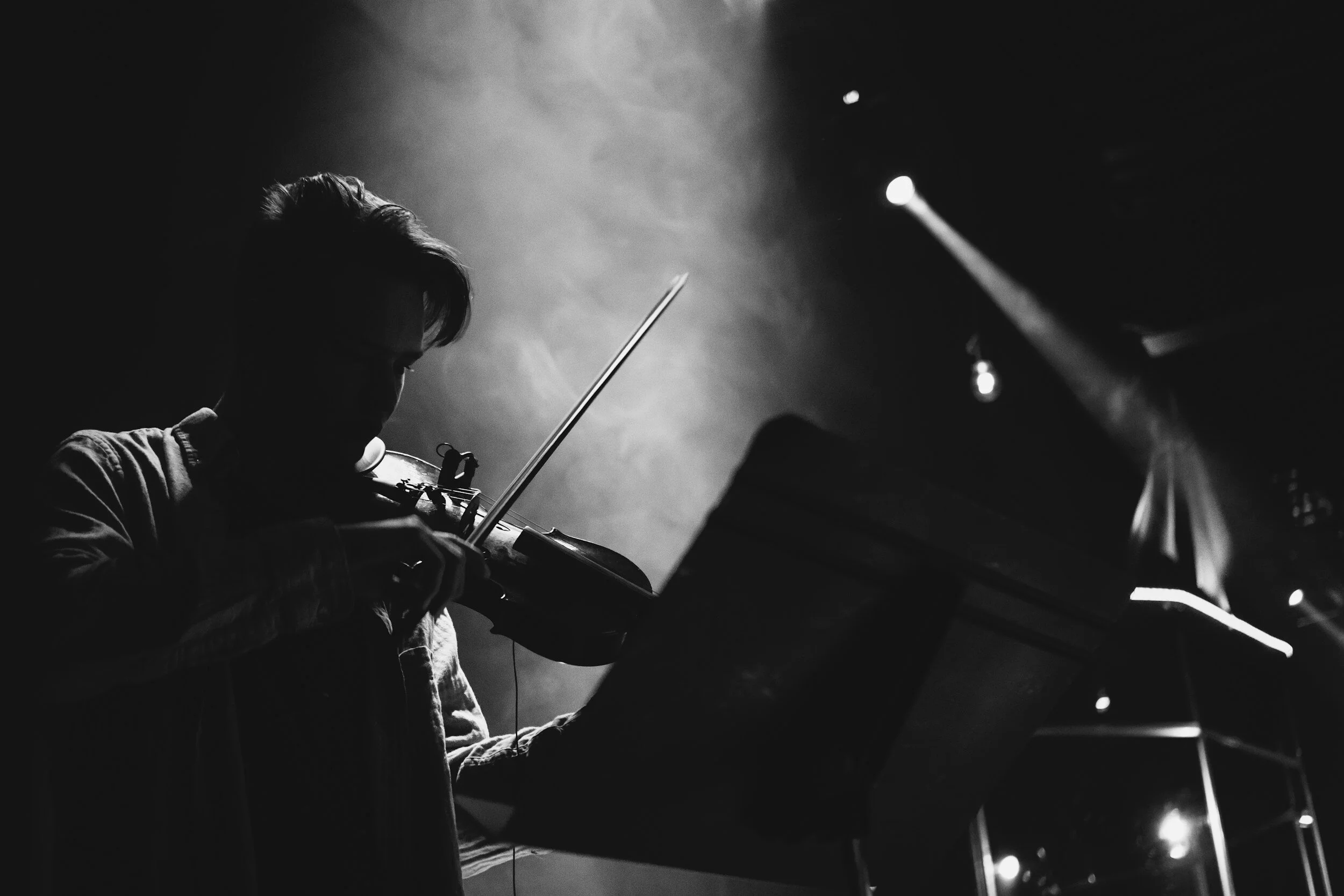 Silhouette of a person playing the violin in a dark setting with spotlight and stage lights