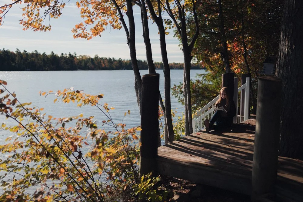 Jacie Targett, spiritual healing and wellness coaching expert, sits on a wooden platform beside a lake.