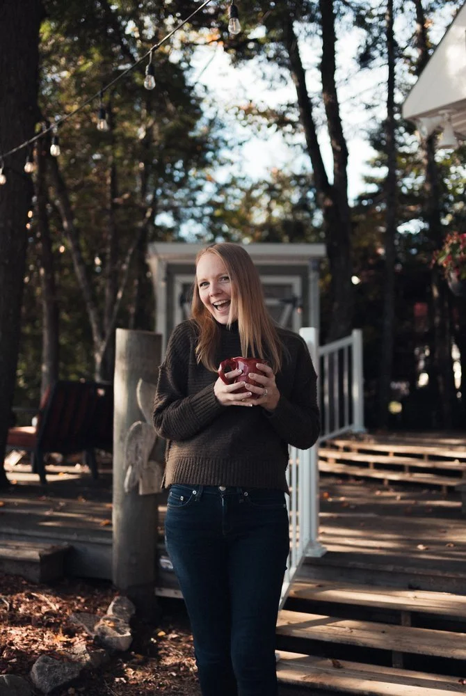 Jacie Targett, Holistic Freedom Coach, sipping a coffee and smiling widely on an autumn day.