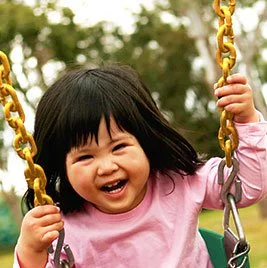 Young child smiling on a swing outdoors.
