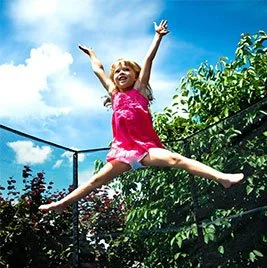 Child jumping joyfully on a trampoline outdoors.