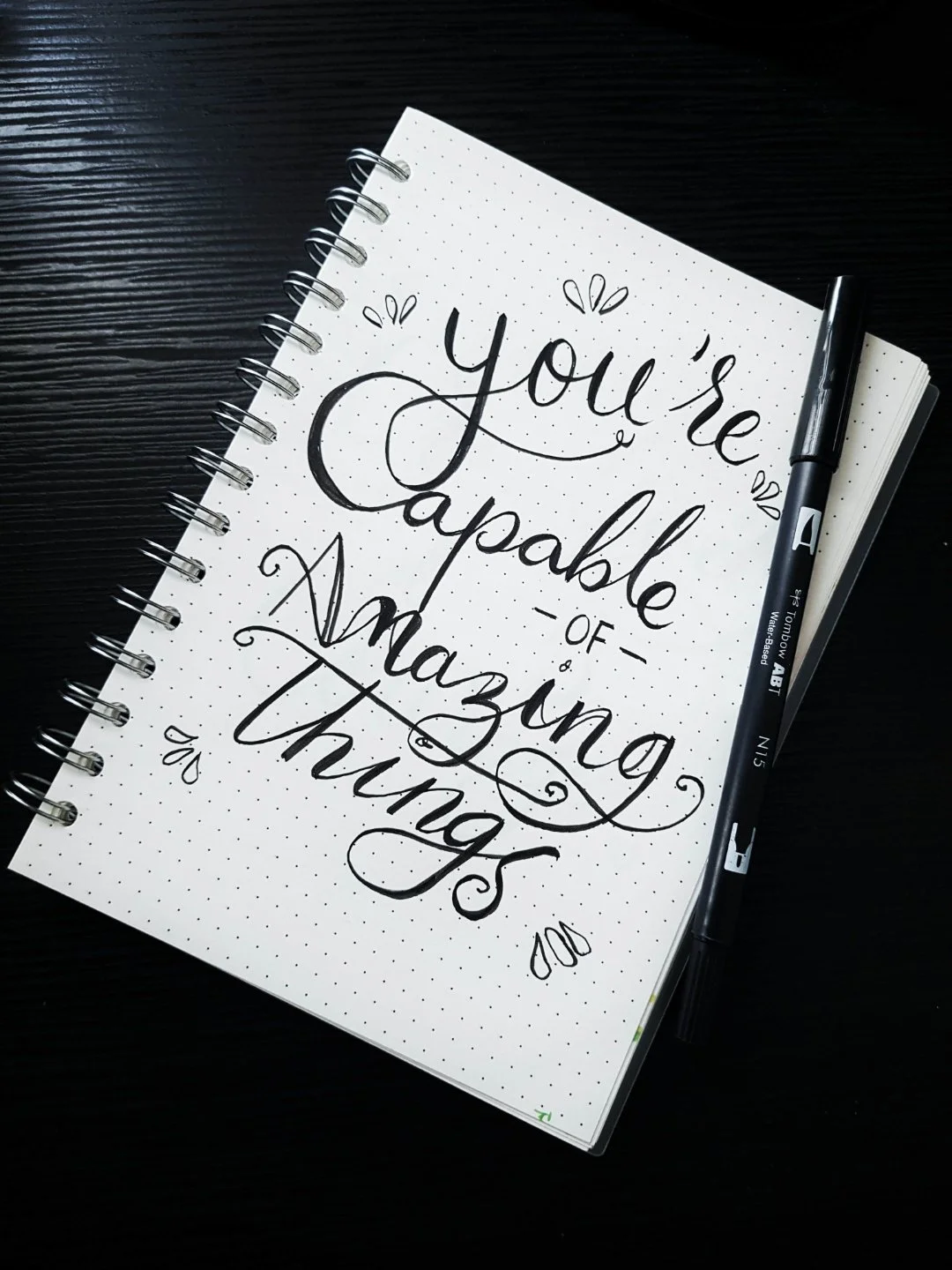 A notebook on a black background with the words "you're capable of amazing things" written in script
