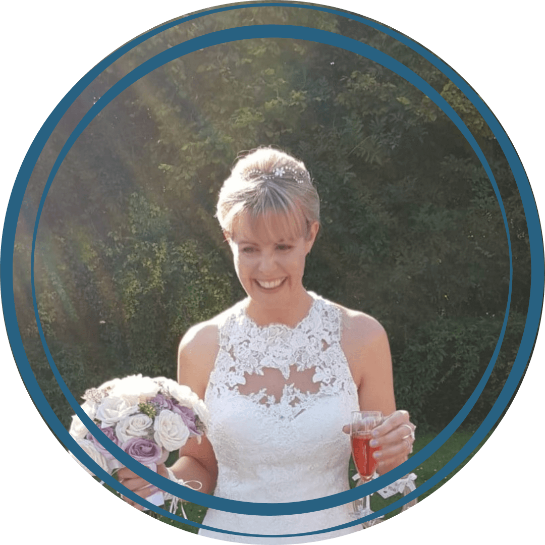 Lady with blonde hair in a white sleeveless wedding dress holding flowers and a glass