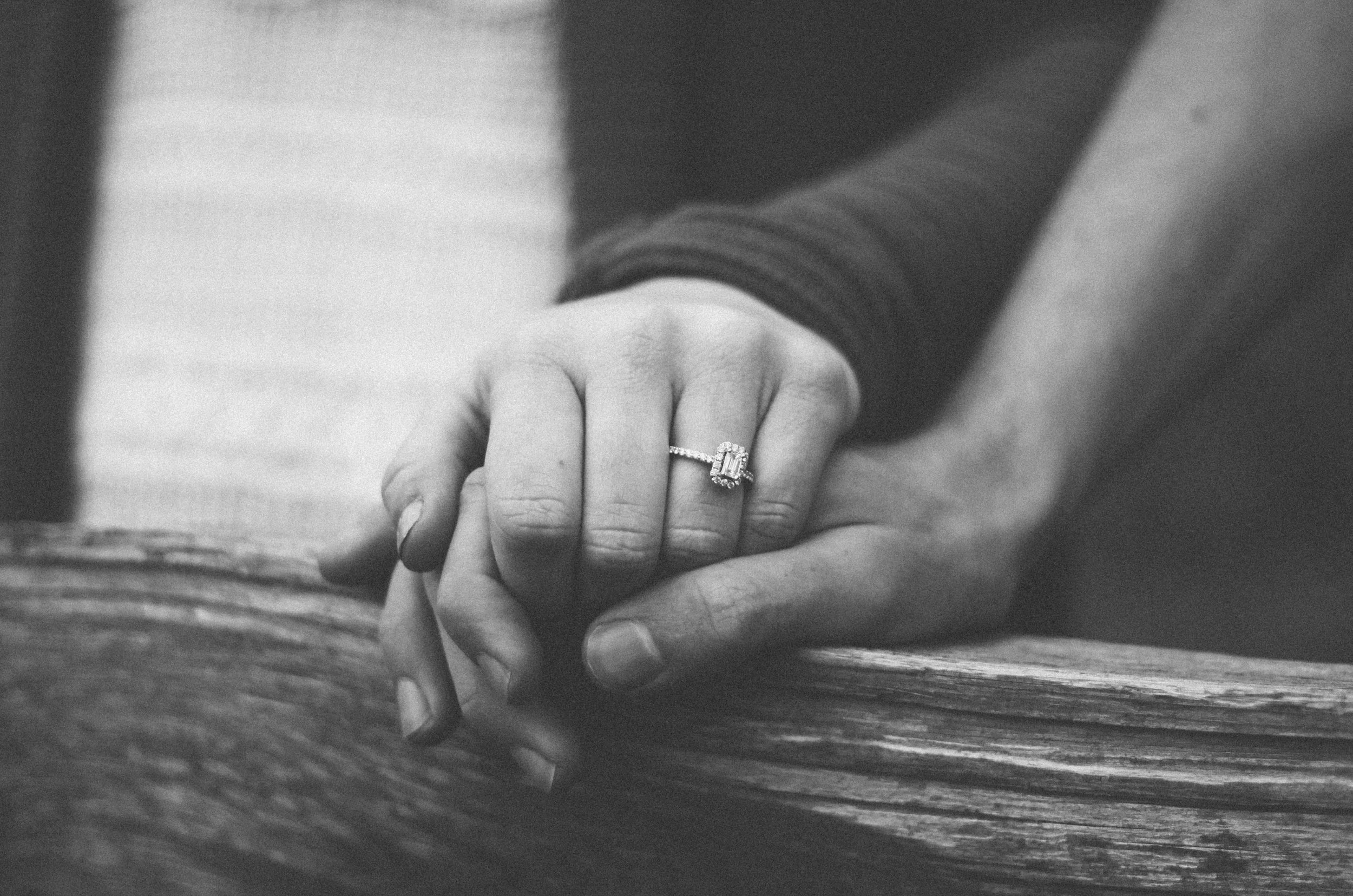 Black and white photo of two hands clasped on a fence line