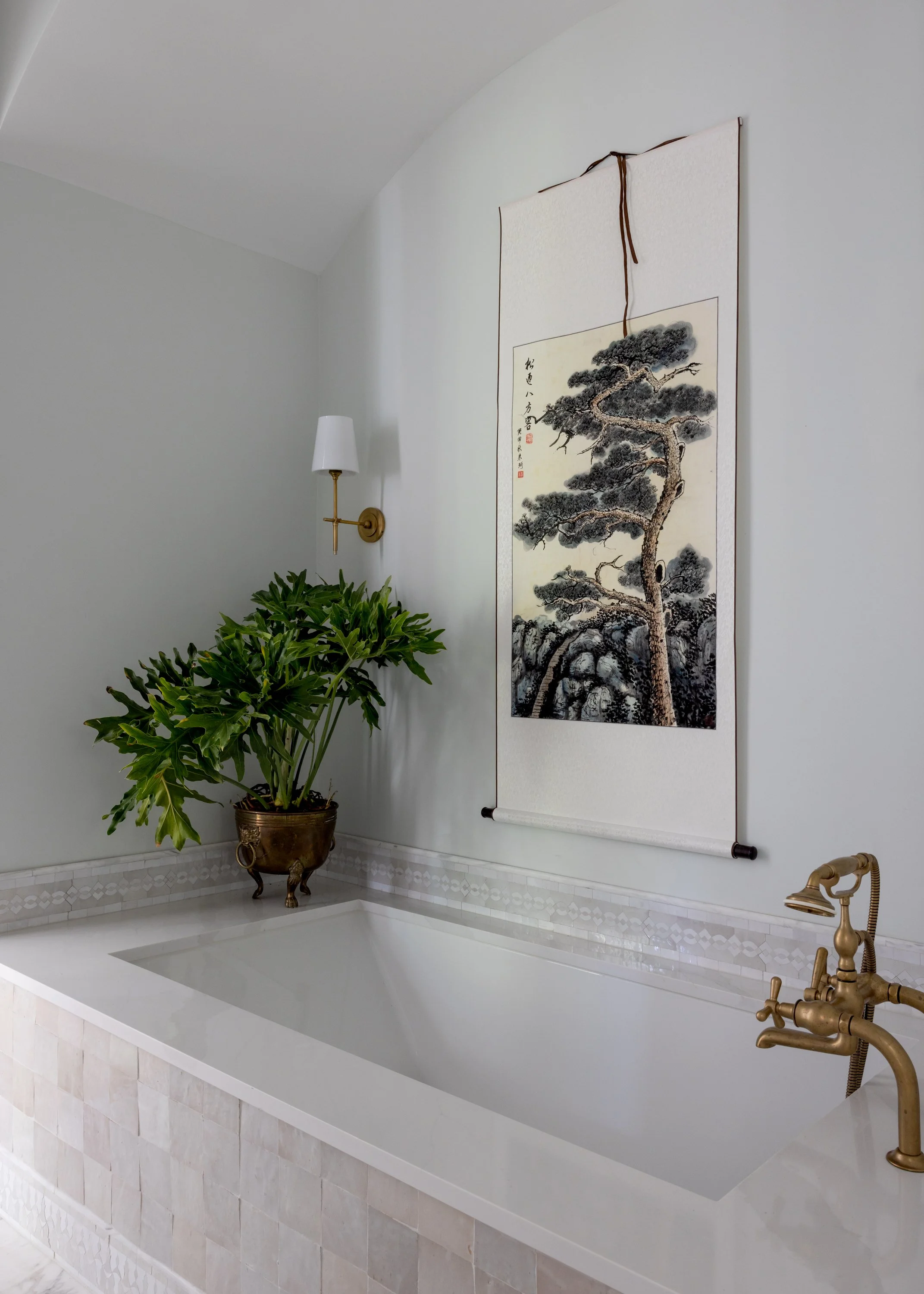 Serene primary bathroom vignette of grey zellige tiled bathtub, unlacquered brass faucet, and Moroccan tile border in Imparfait-designed space Crawford