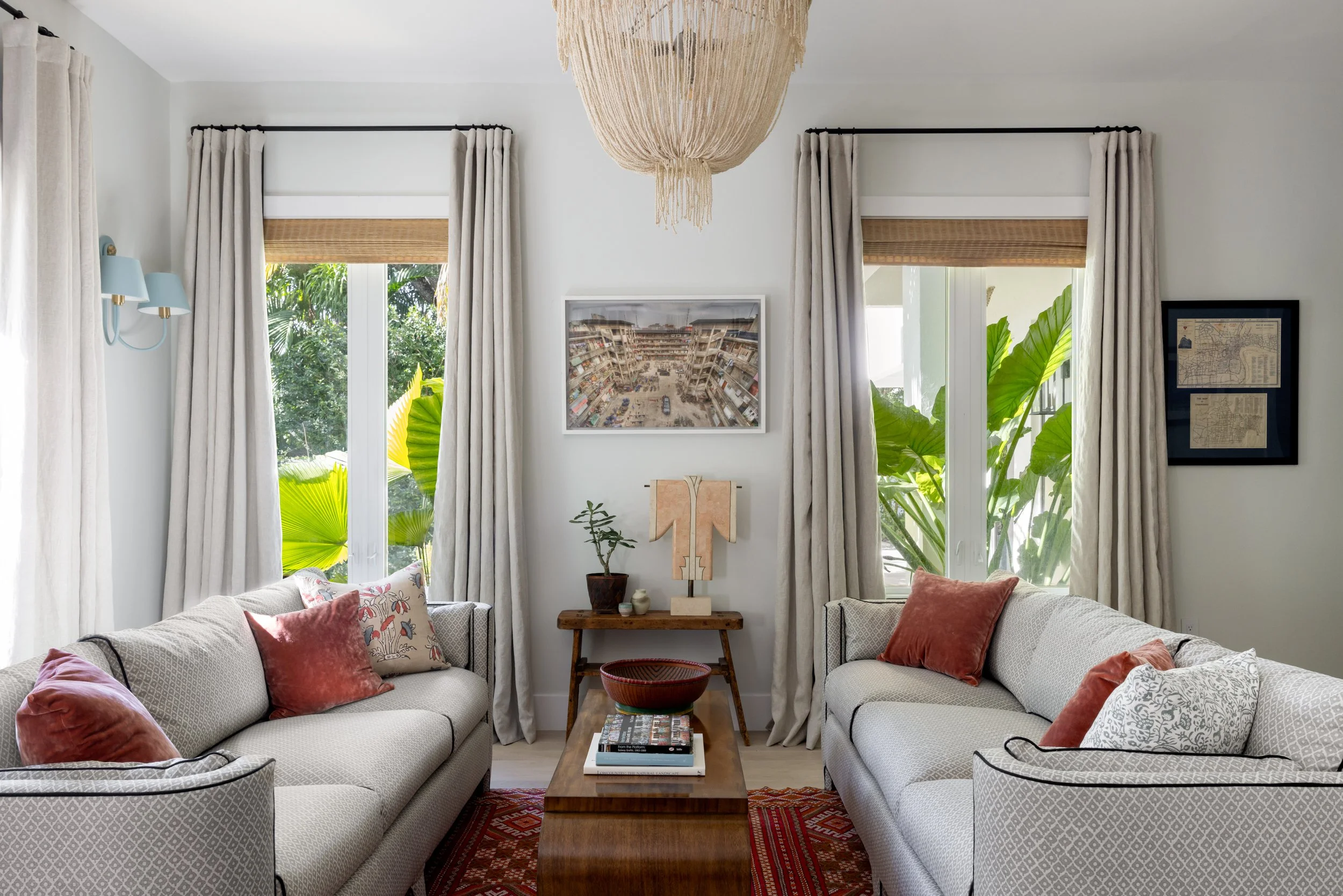 Chic seating area in primary bedroom with tapestry chandlier, pastel blue sconces, white and grey patterned sofas with black piping, Chinese coffee table, and a red patterned rug inside Imparfait Design Studio-designed Crawford