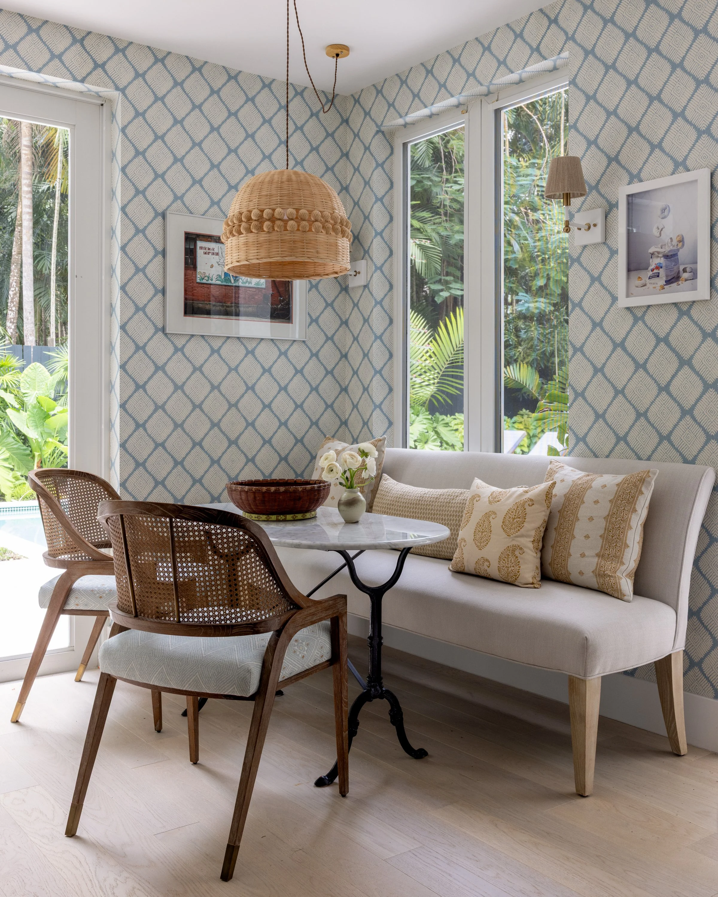 Cozy breakfast nook with an off-white linen banquette, marble bistro style table, curved rattan chairs with light blue patterned upholstery, and a woven light fixture in Imparfait designed space Crawford