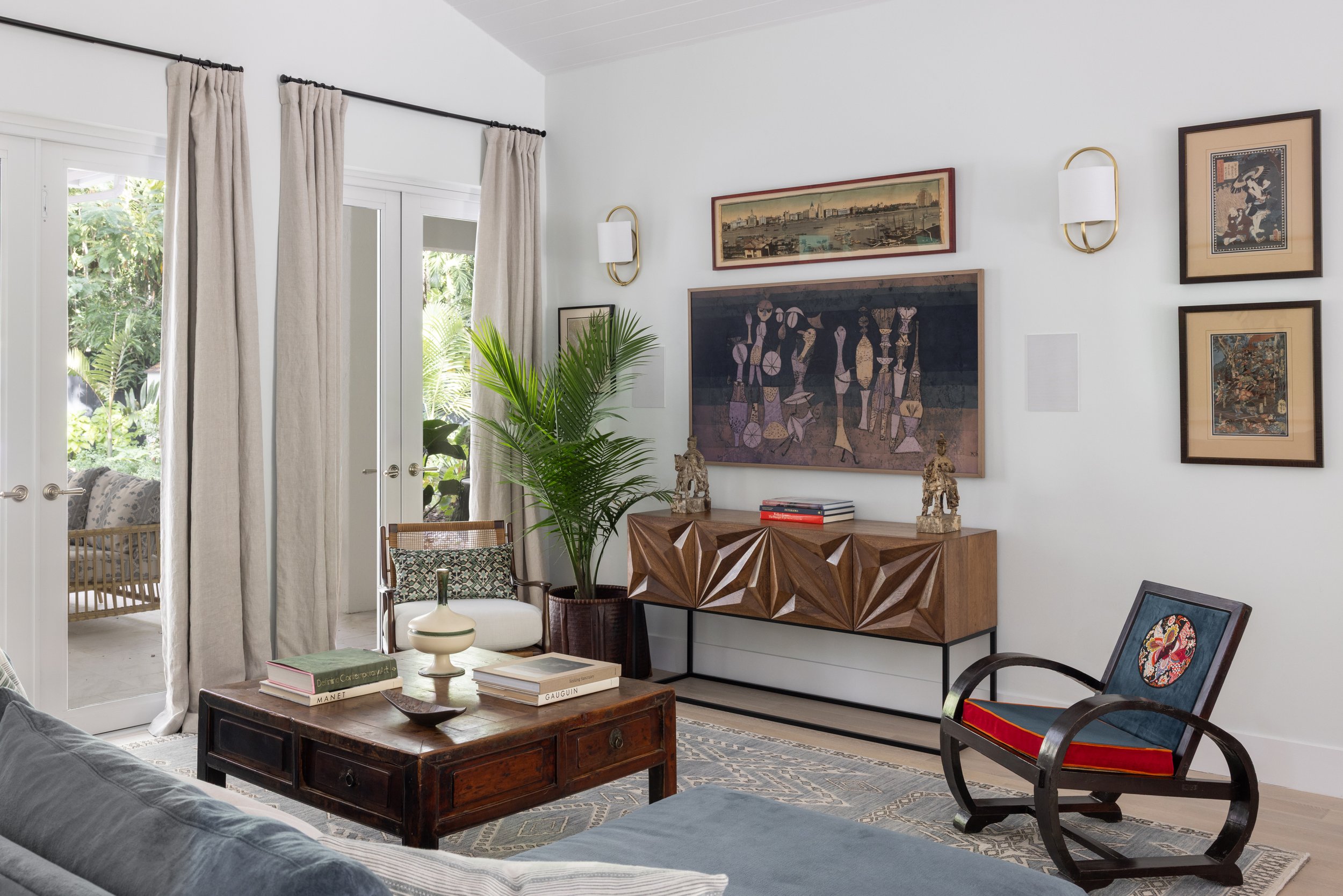 Another view of the main living room with a Ming coffee table, a rattan curved Ming style chair, and black bentwood Art Deco rocking chair with a blue and red cushion, a wooden architectural console, and an array  in Imparfait-designed space Crawford