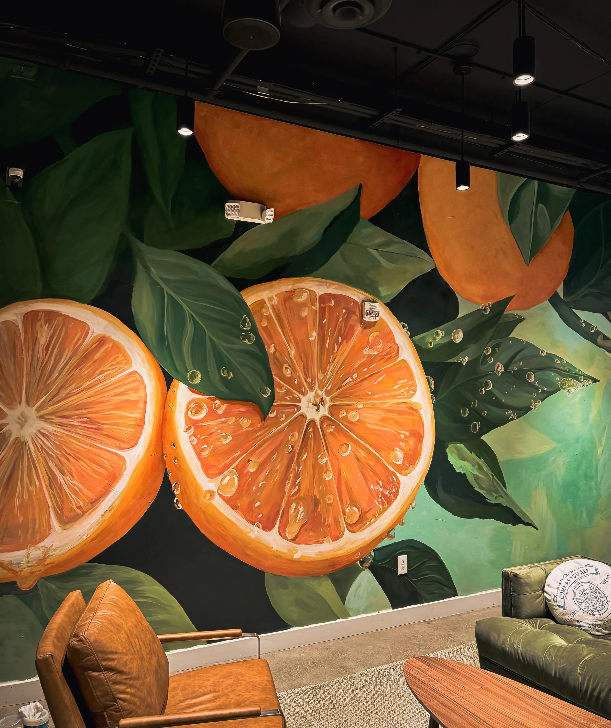 A vibrant mural of sliced oranges surrounded by green leaves, with water droplets on the fruit and leaves.