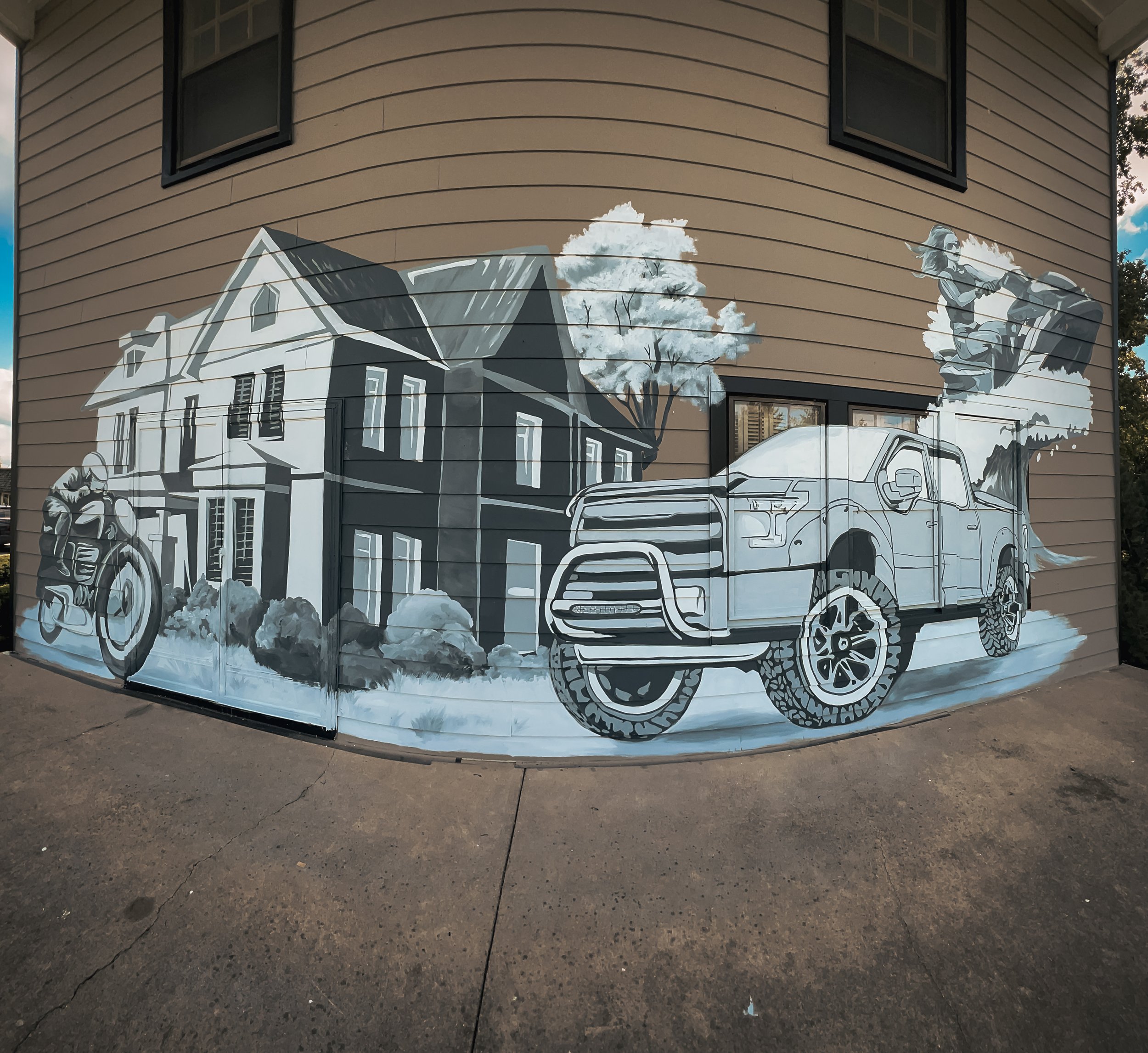 Monochrome exterior mural wrapping around a commercial insurance building with a house, pickup truck, motorcycle, trees, and outdoor imagery.
