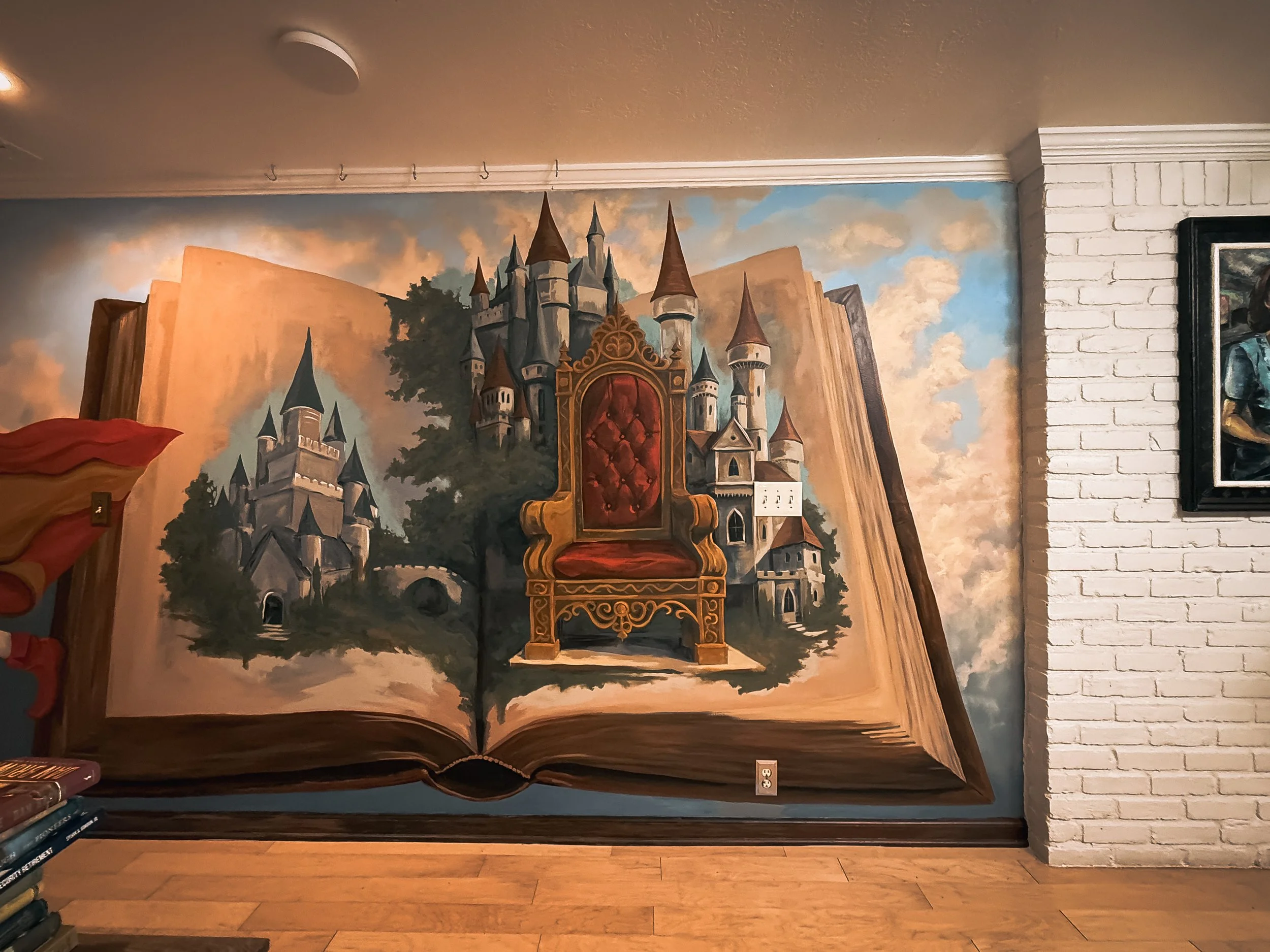 Storybook Castle Interior Mural
Whimsical interior mural featuring an open storybook with a painted castle and ornate red-and-gold throne against a cloud-filled sky.