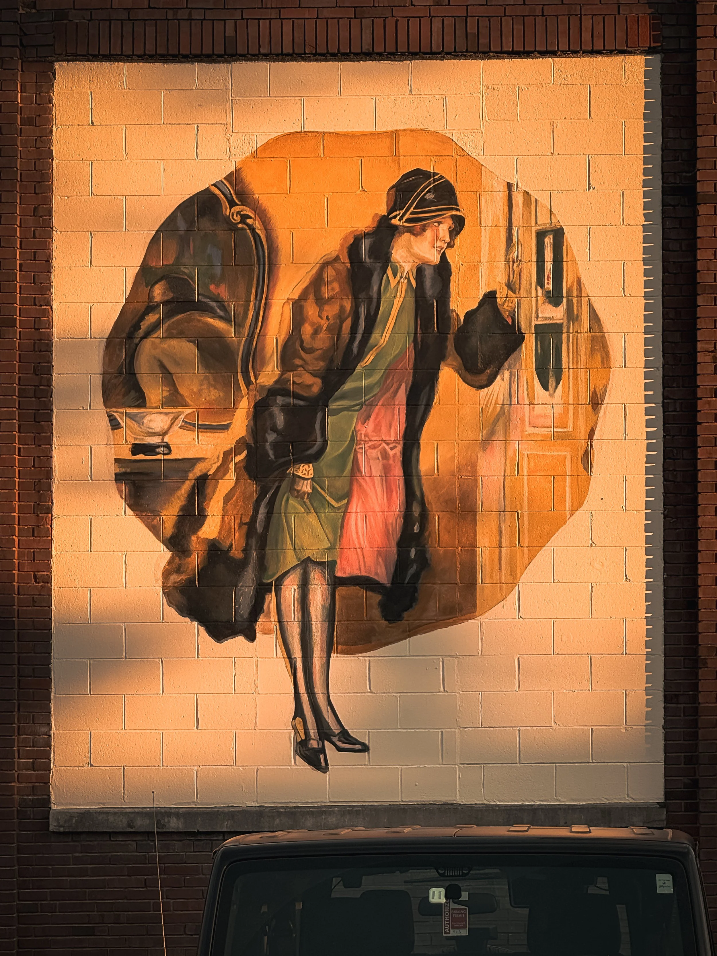 A mural on a brick wall depicting a woman in high heels, wearing a jacket, a green shirt, and red pants, with a reflective surface in front of her.