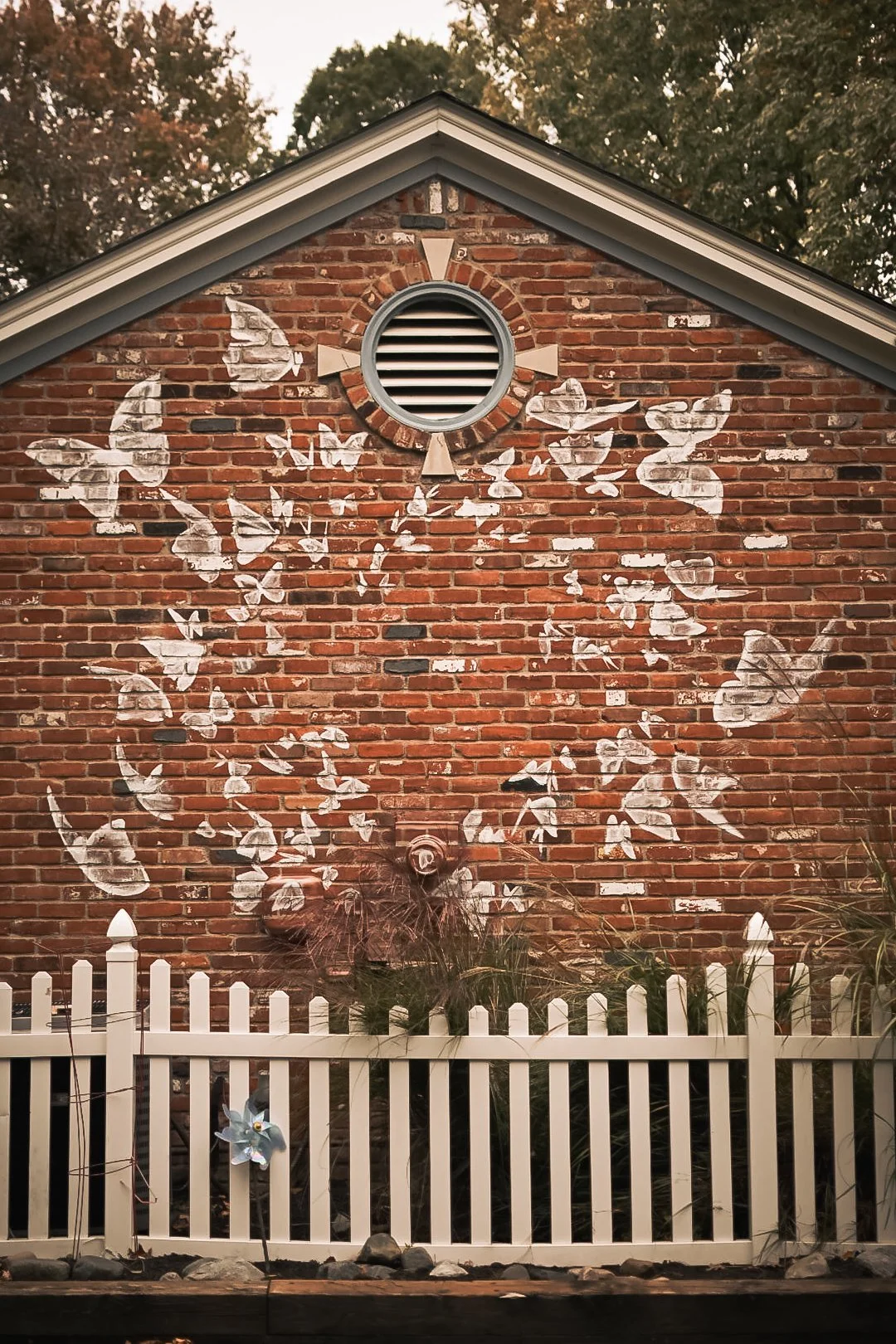 Exterior brick mural featuring a flock of white butterflies spreading across a residential garden wall.