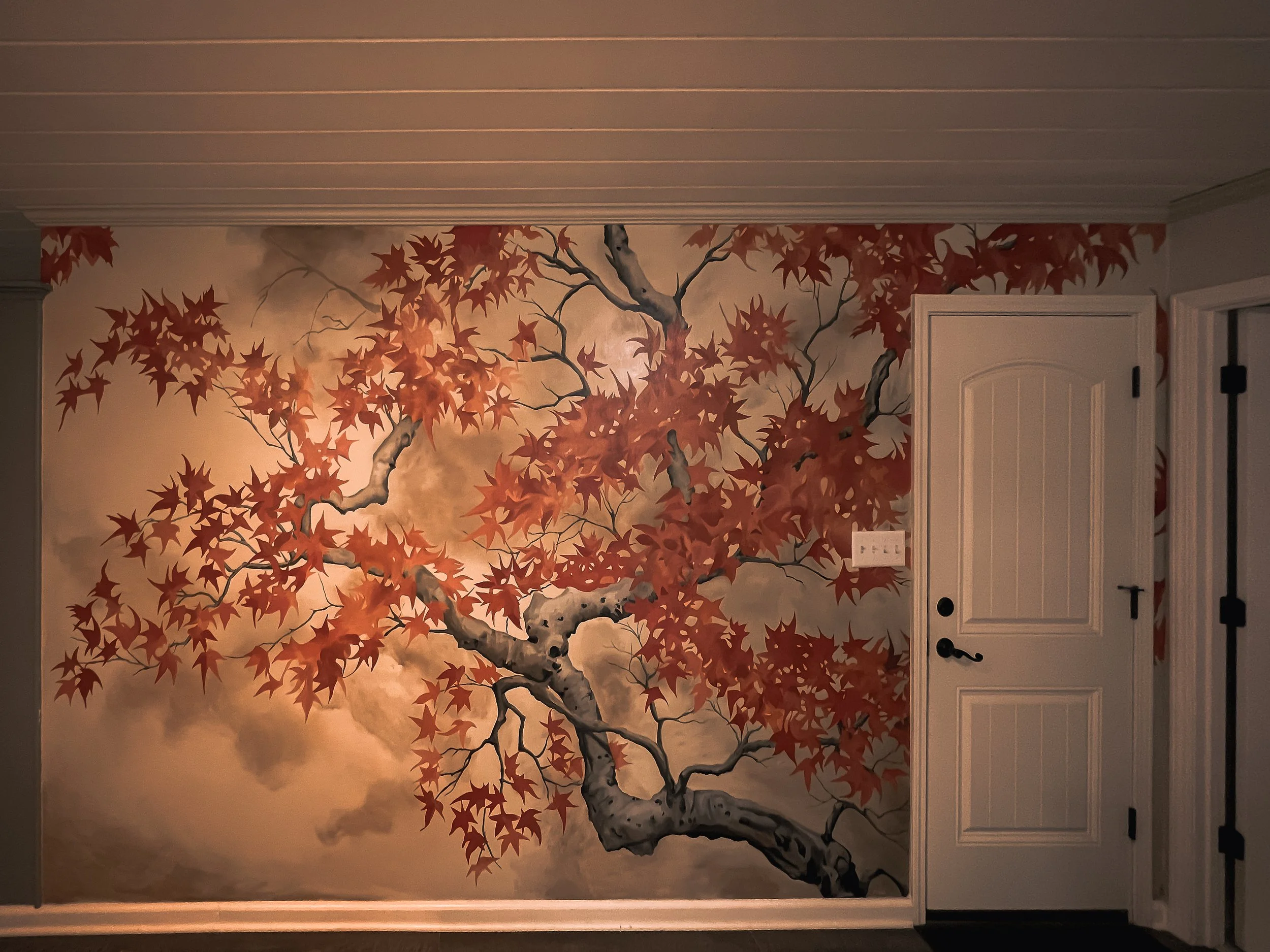 A painted mural of a tree with red autumn leaves on a beige background, located on a wall near a white door.