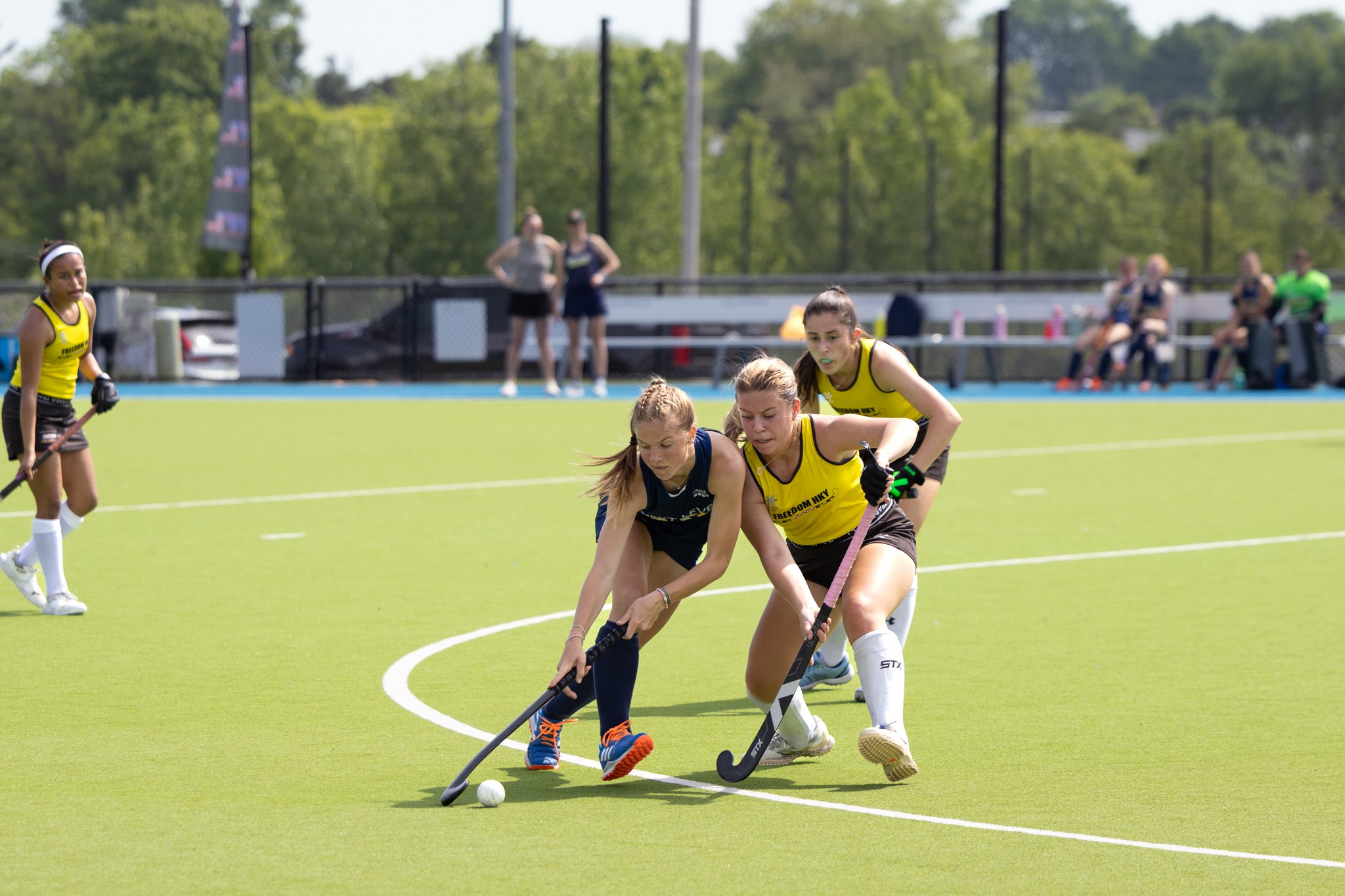 Field hockey player dribbling the ball as a defender is running next to her
