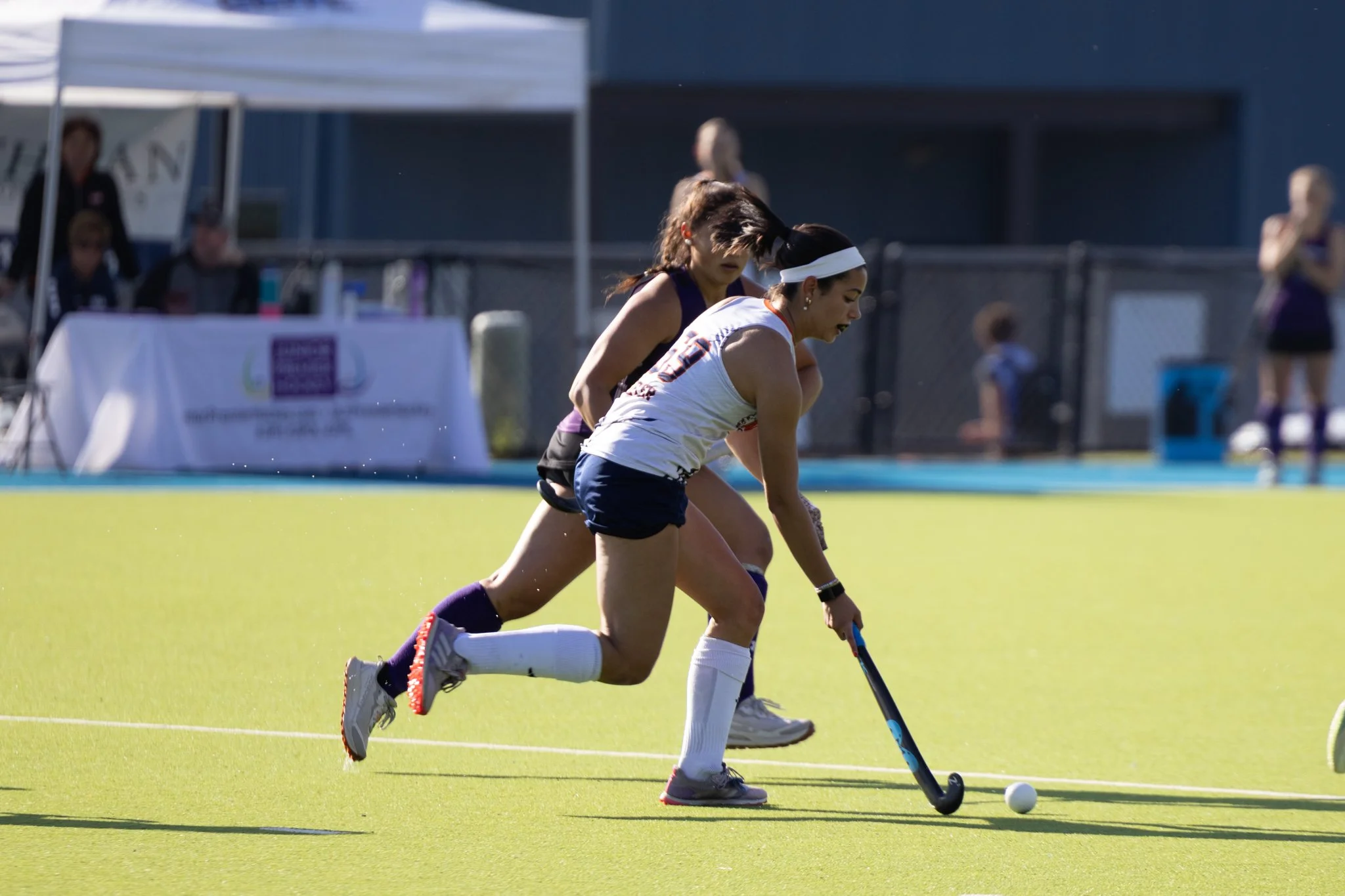 Field hockey player dribbling the ball as a defender is running next to her