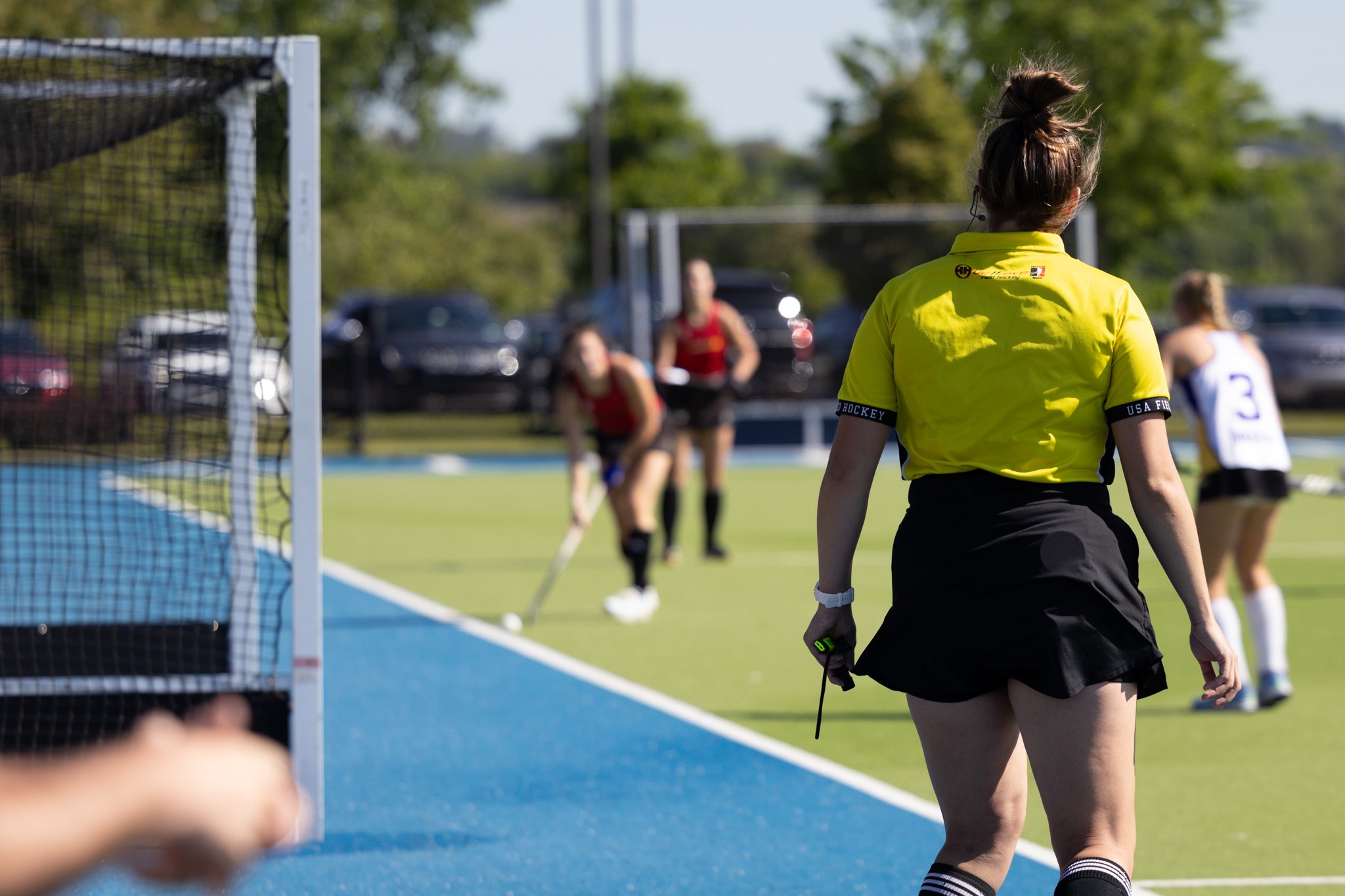 Field hockey referee standing with players in the background