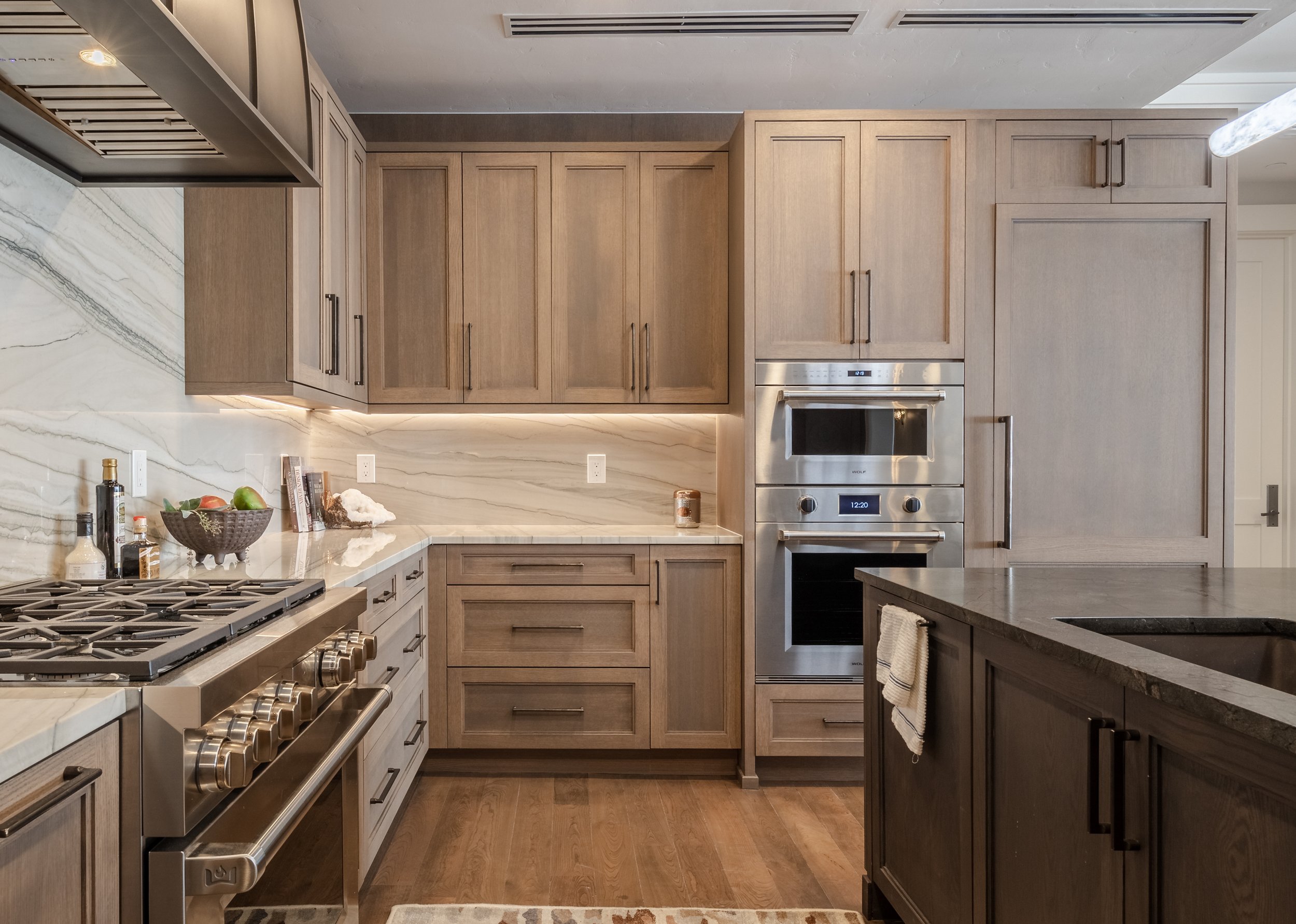 Modern kitchen with light wood cabinets, stainless steel appliances, marble backsplash, and a dark countertop.