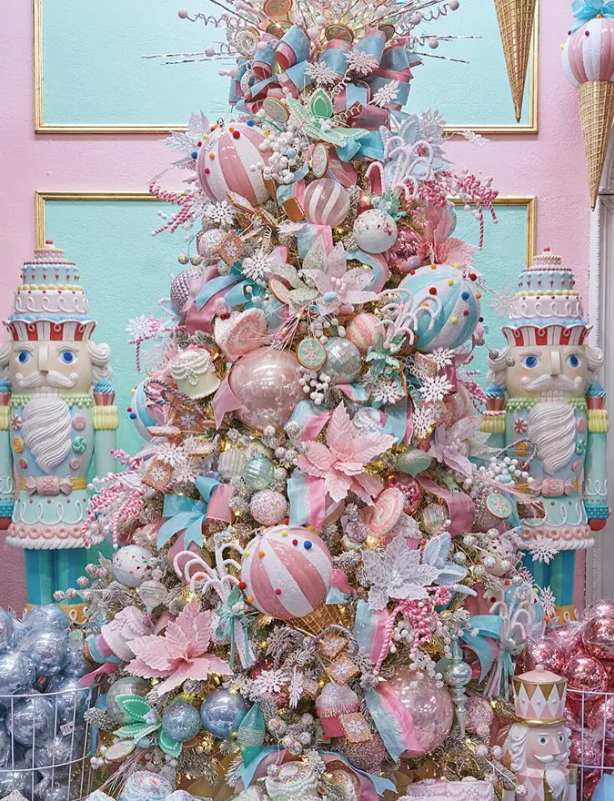 Decorative Christmas tree with pastel pink, blue, and white ornaments, ribbons, and glitter, flanked by two nutcracker figures.