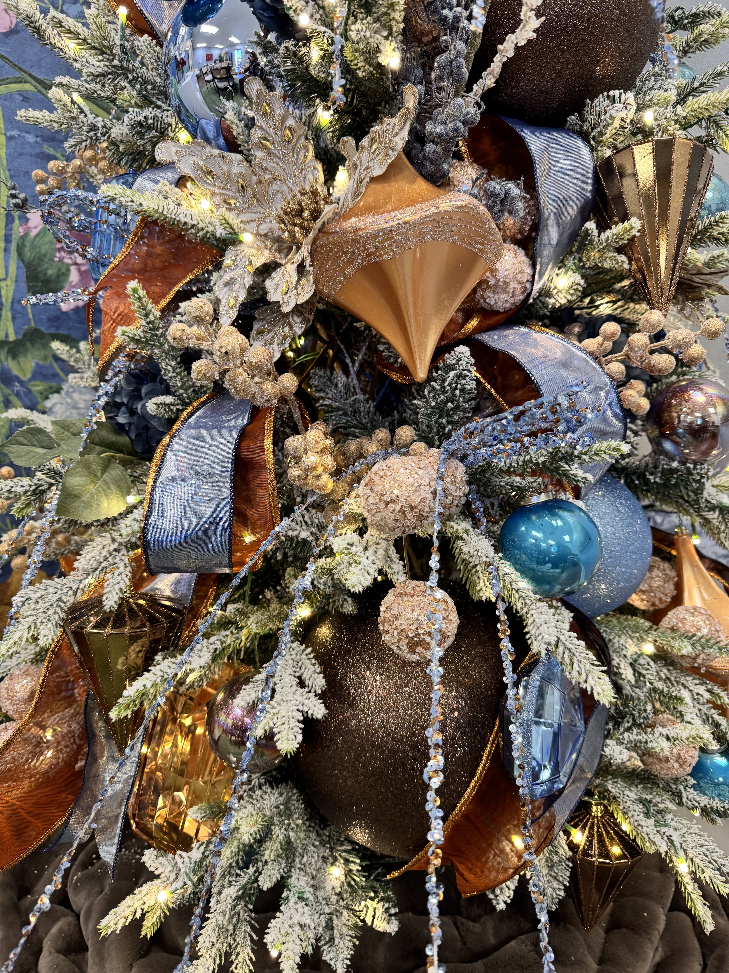 Close-up of a decorated Christmas tree with ornaments in gold, silver, black, and blue, including ribbons, baubles, and lights.