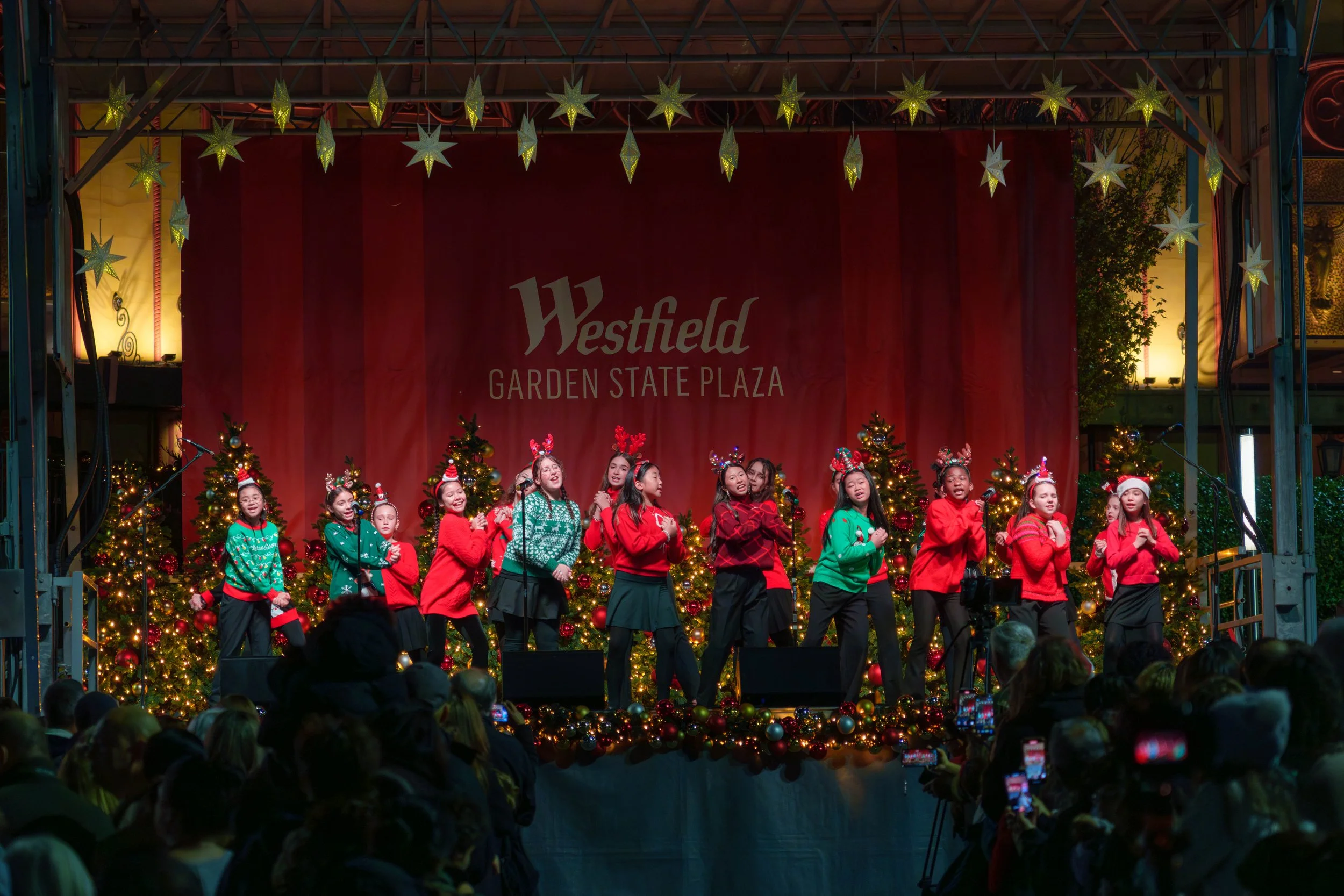 A group of children performing a dance on a decorated Christmas stage at Westfield Garden State Plaza during the holiday season.