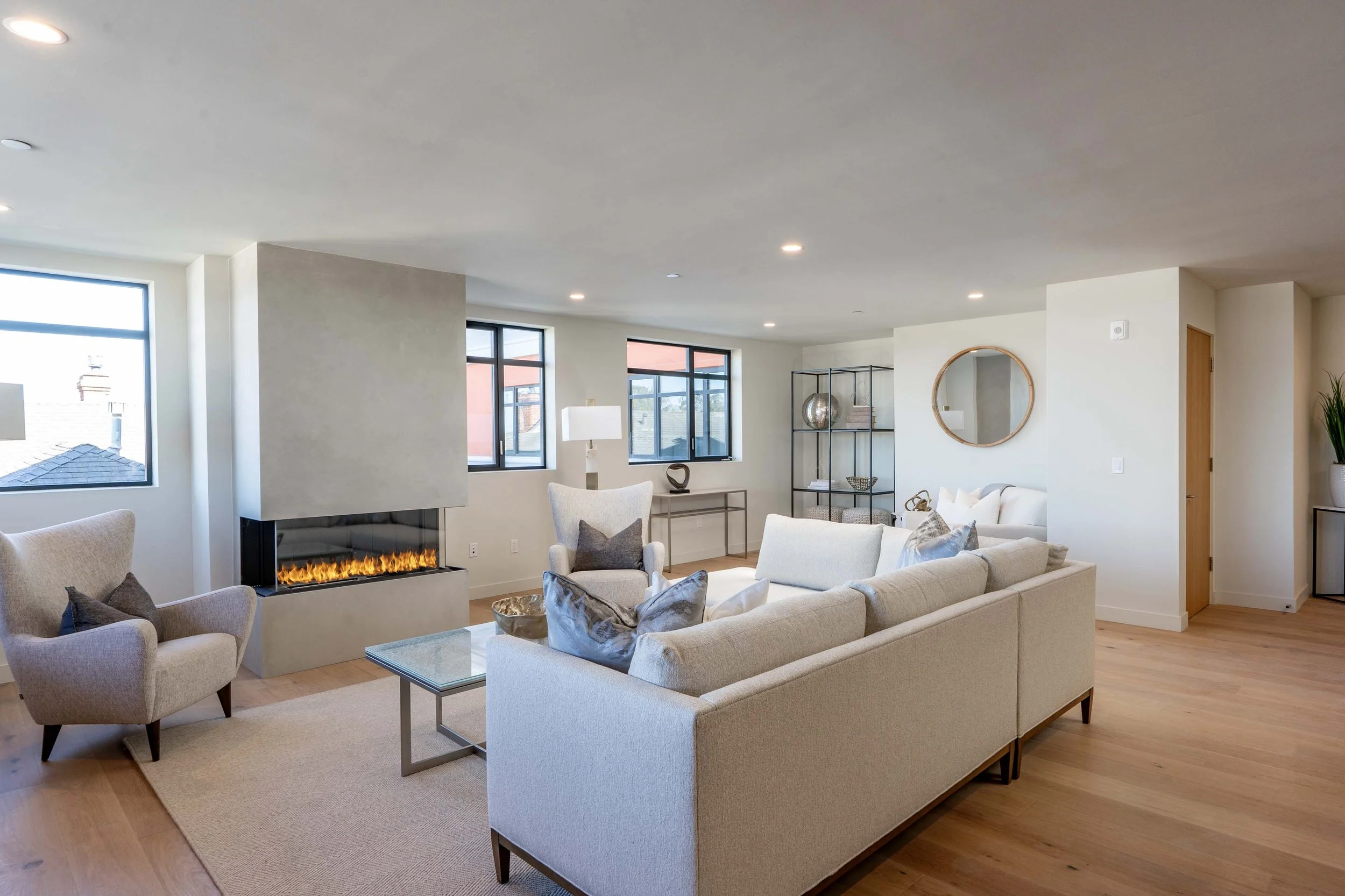 Modern living room with white sofas, a beige armchair, a fireplace, large windows, and decorative items.