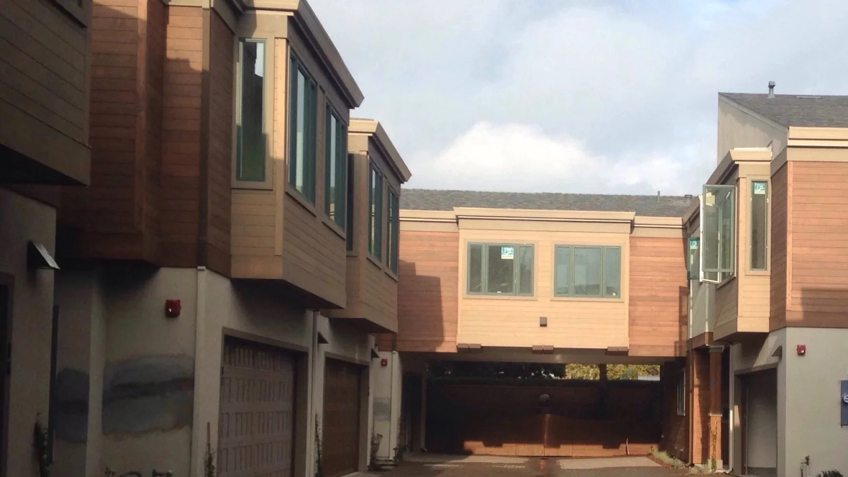 View of a parking area beneath residential buildings with brown and beige exteriors, windows, and a blue trash bin, taken in the morning at 9:33 AM.