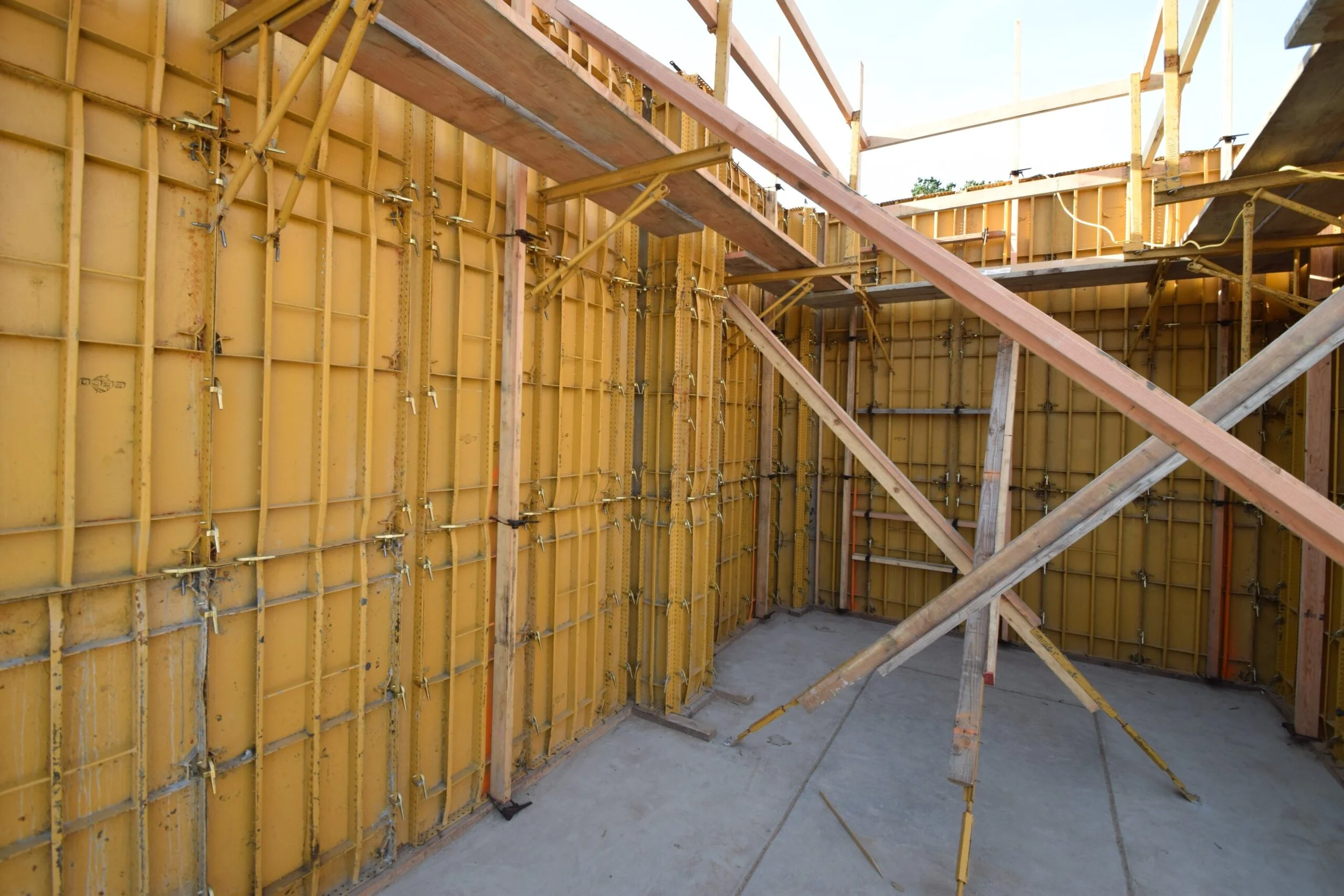 Interior of a construction site showing yellow formwork panels and wooden scaffolding for pouring concrete walls.