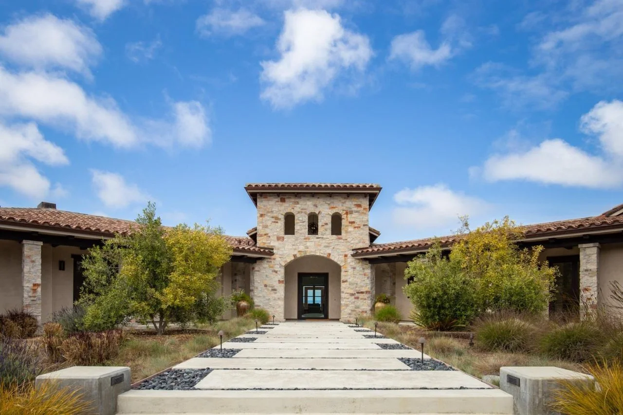 Front view of a modern house with a stone façade, surrounded by desert landscaping and a clear blue sky.
