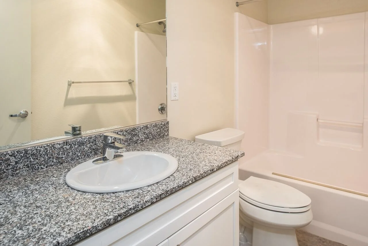 Bathroom with granite countertop sink, mirror, toilet, and bathtub with shower walls.